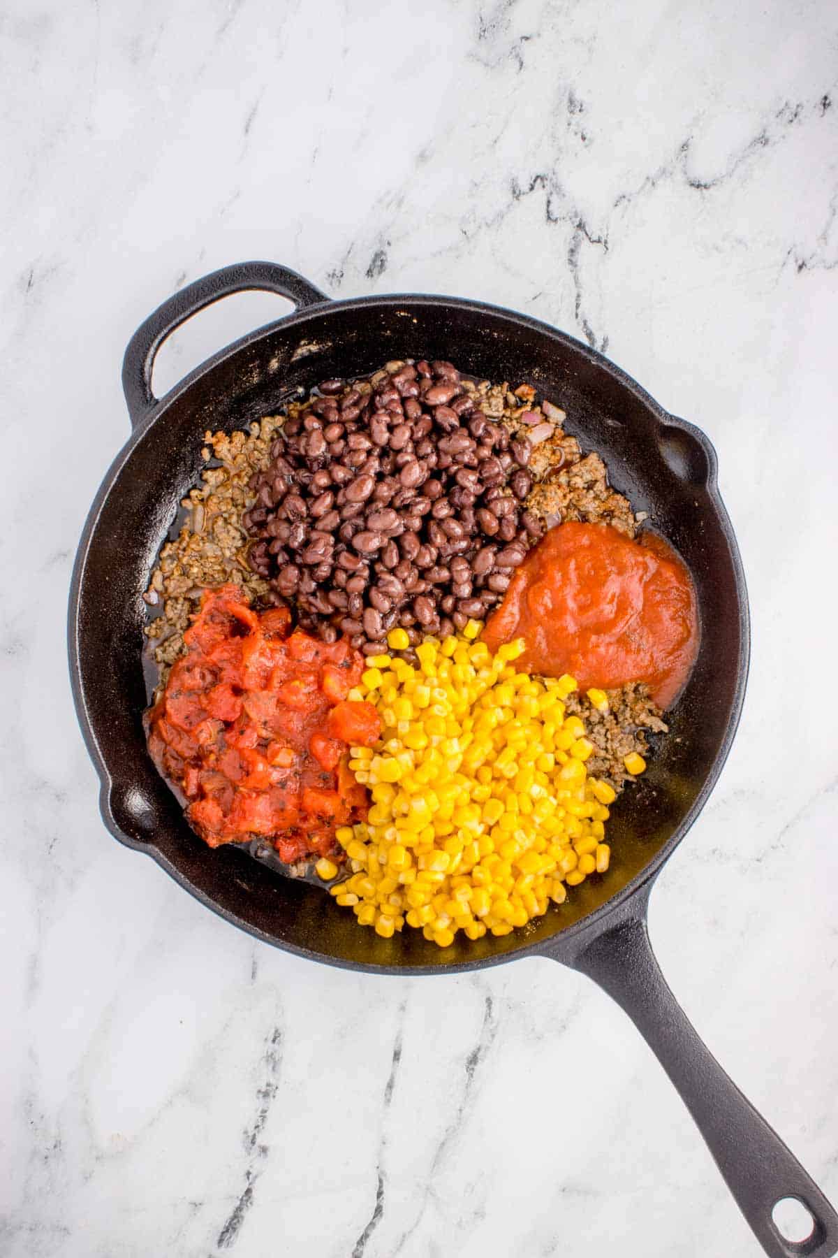 black beans, diced tomatoes, corn and tomato sauce on top of ground beef in a skillet