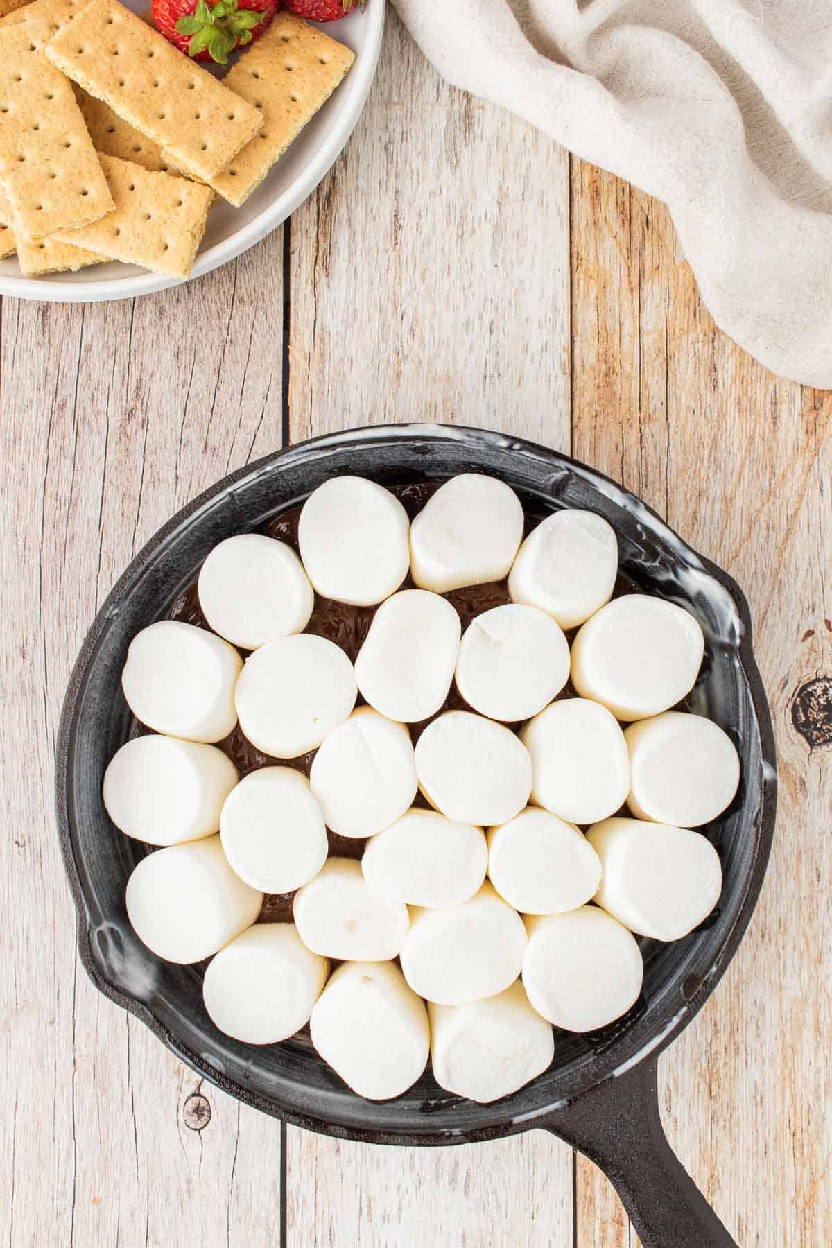 marshmallows on top of melted chocolate mixture in a cast iron skillet