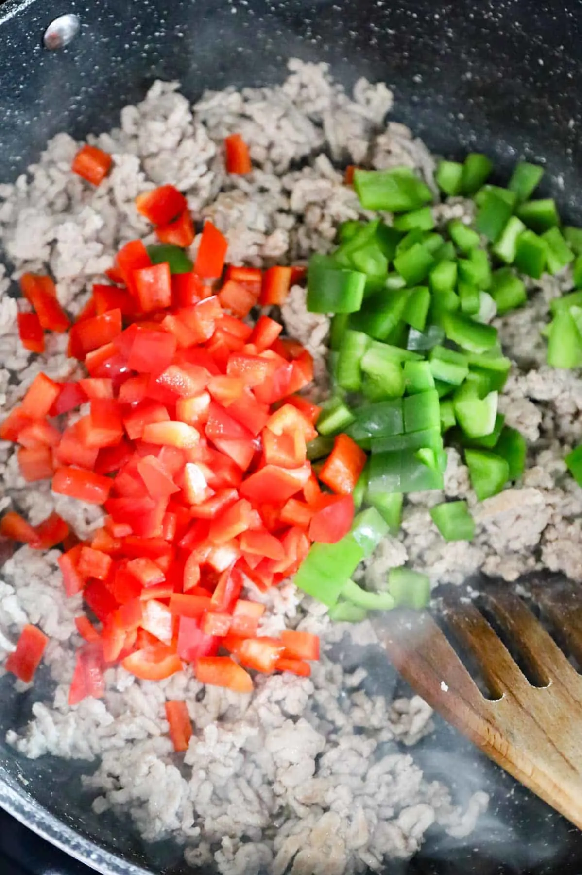 diced red and green bell peppers on top of cooked ground chicken in a skillet