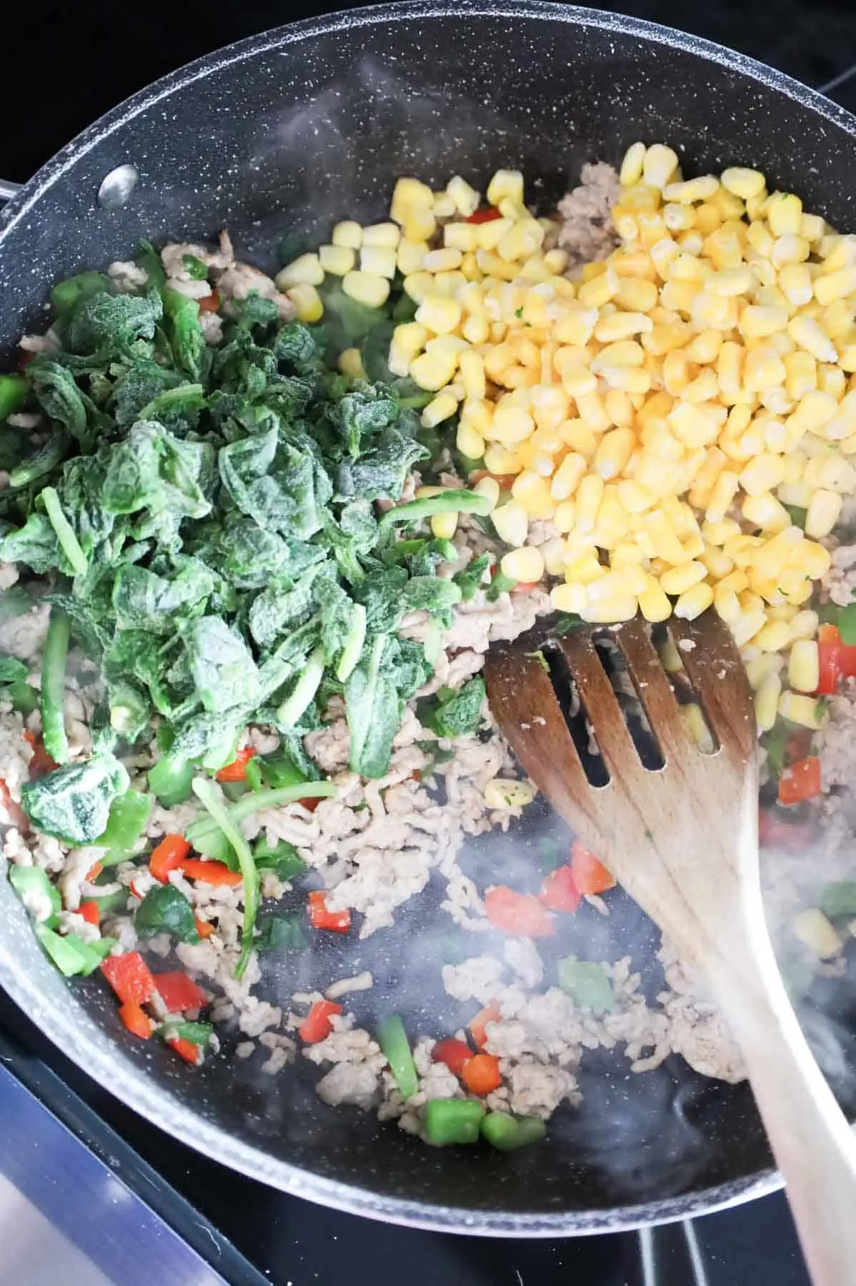 frozen chopped spinach and corn on top of ground chicken and bell pepper mixture in a skillet