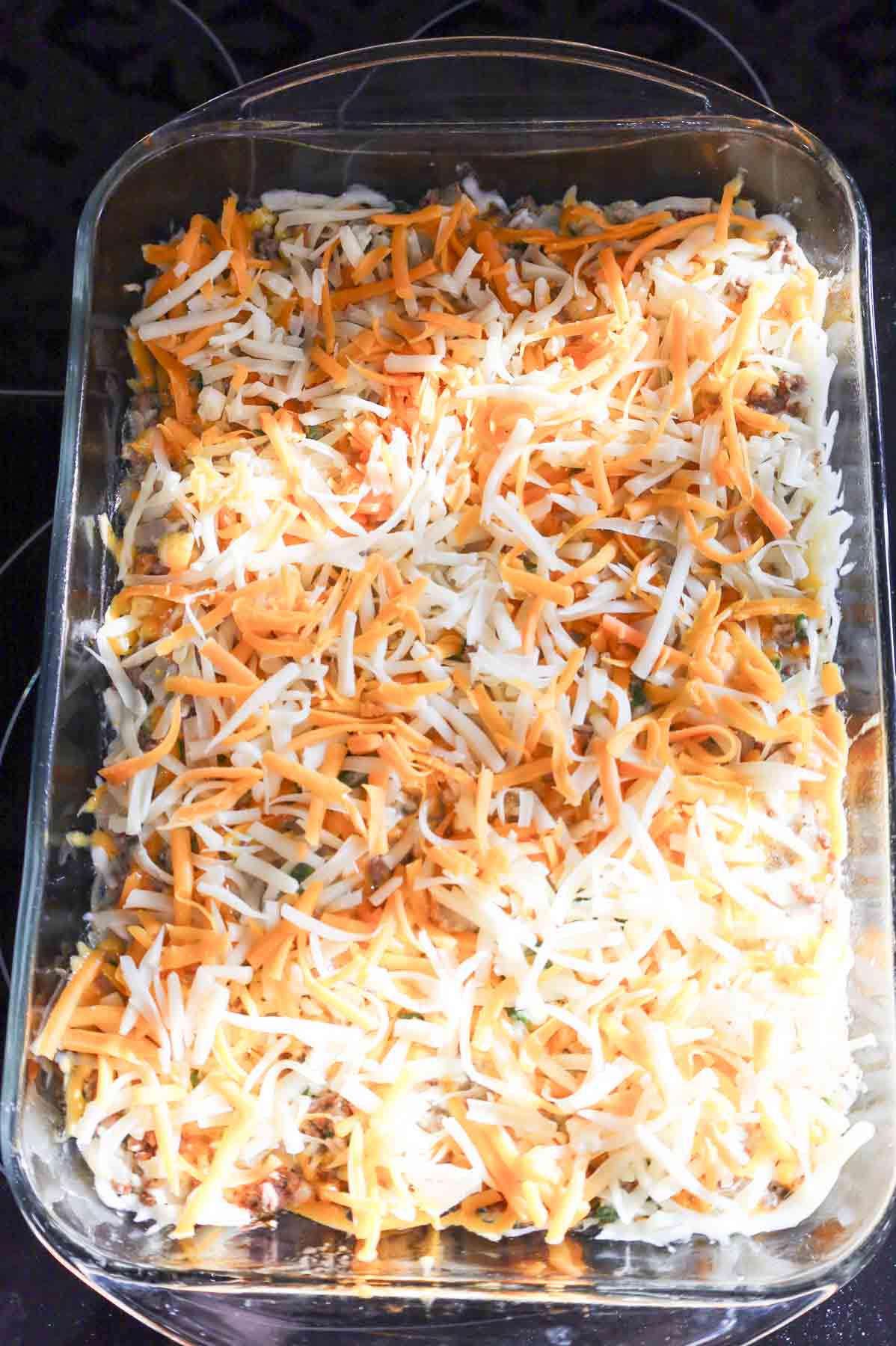 shredded cheese on top of creamy ground beef mixture in a baking dish