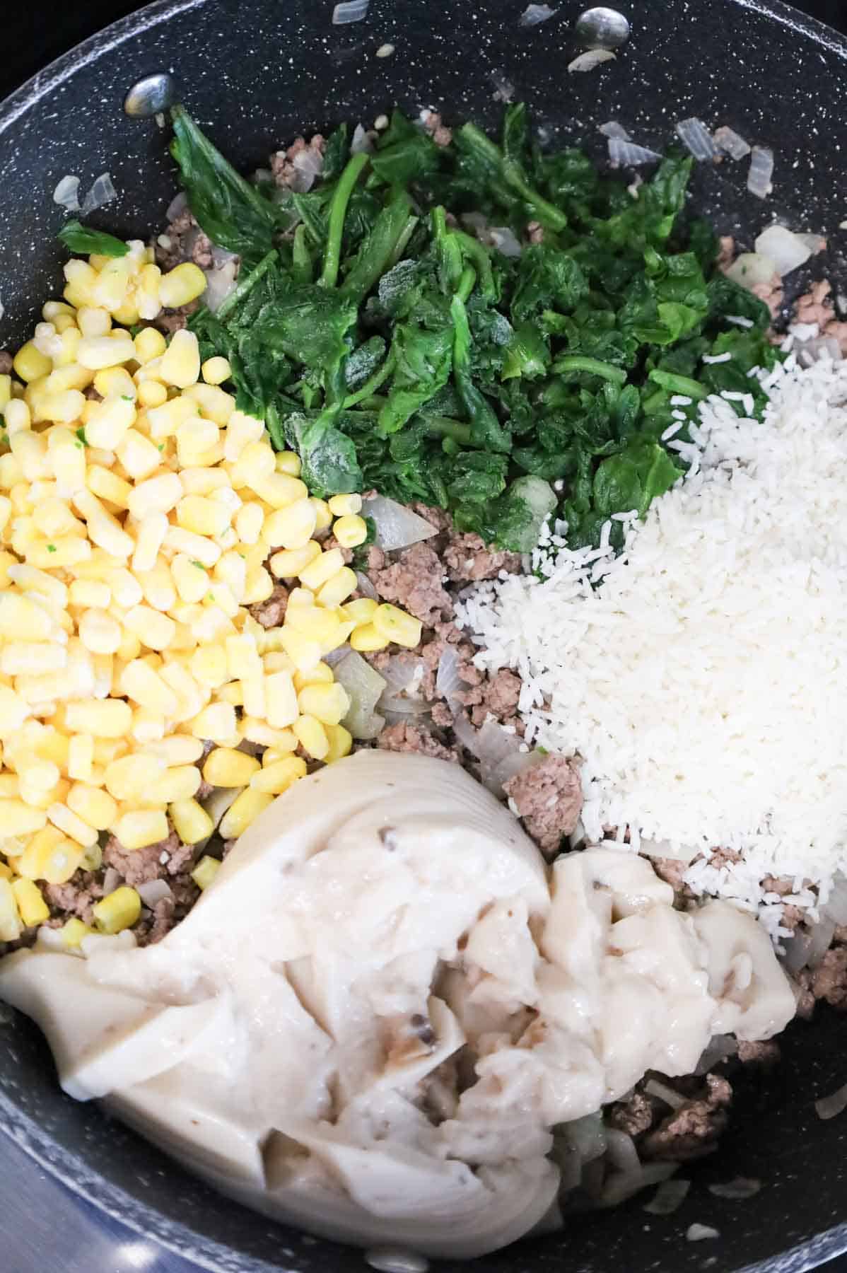 frozen corn, chopped spinach, instant rice and cream of mushroom soup on top of cooked ground beef in a skillet