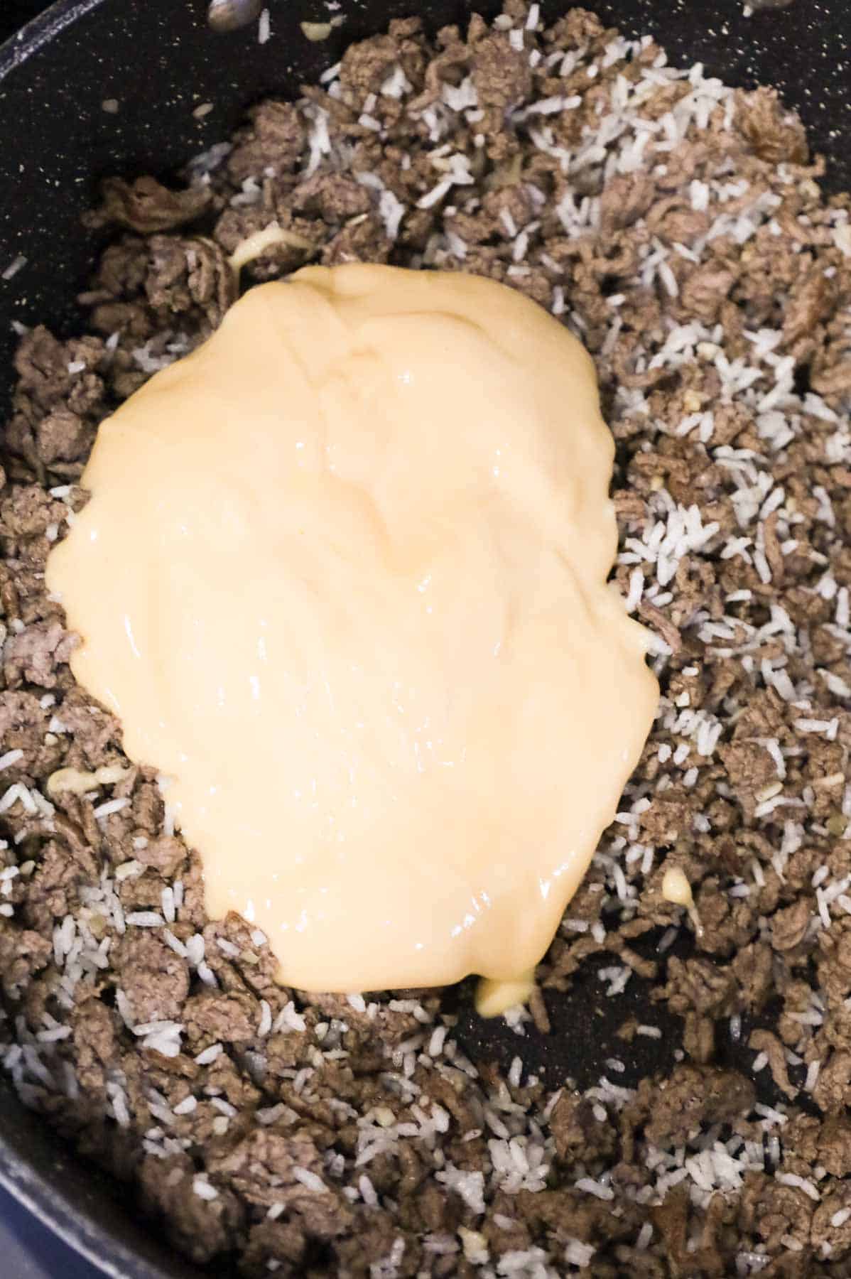 cheddar cheese soup on top of cooked ground beef in a skillet