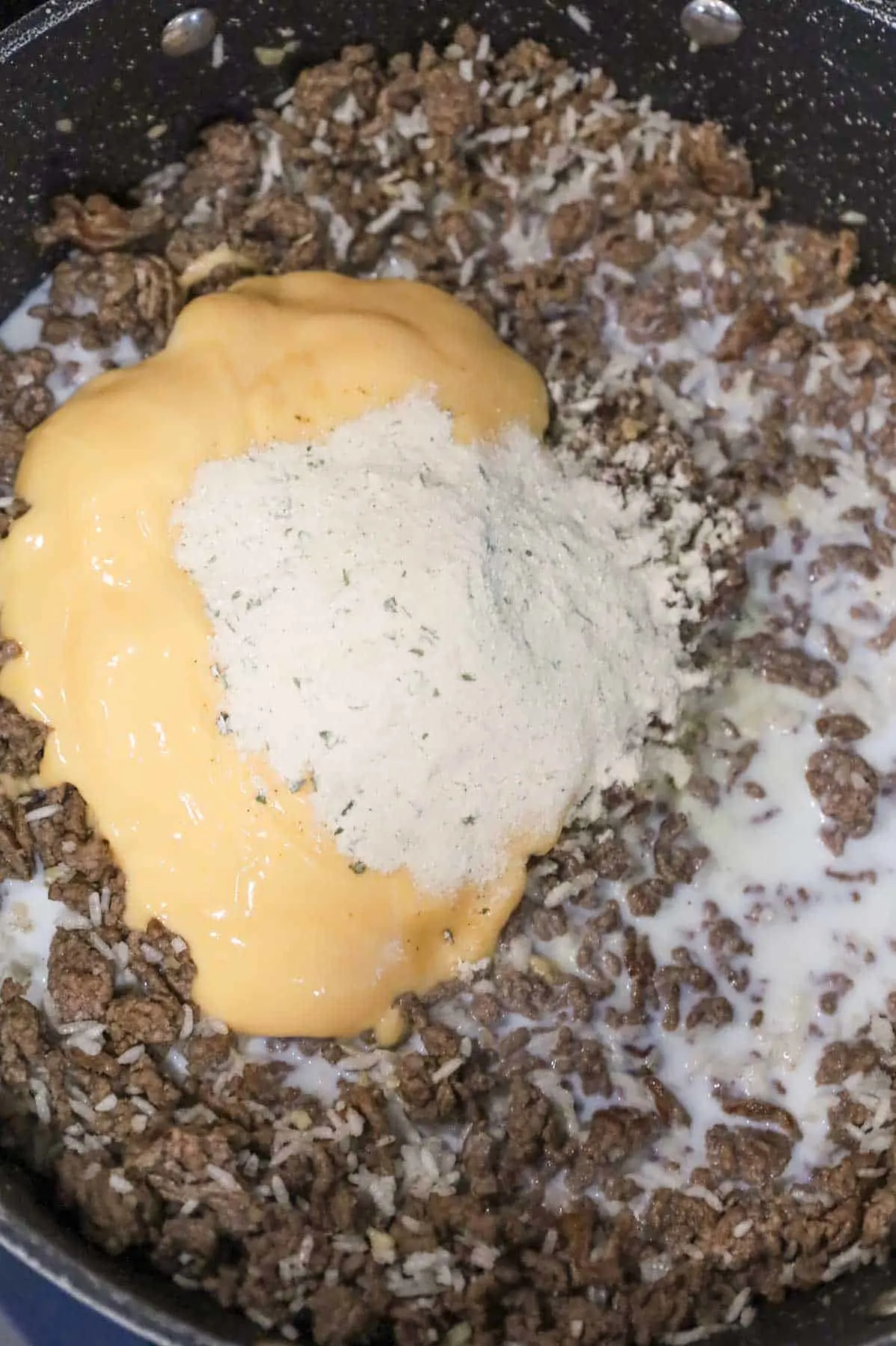 ranch seasoning packet on top of cheddar cheese soup, milk and cooked ground beef in a skillet