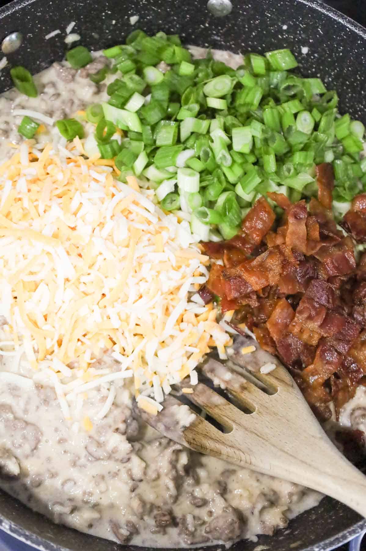 shredded cheese, chopped green onions and cooked bacon pieces on top of creamy ground beef mixture in a skillet