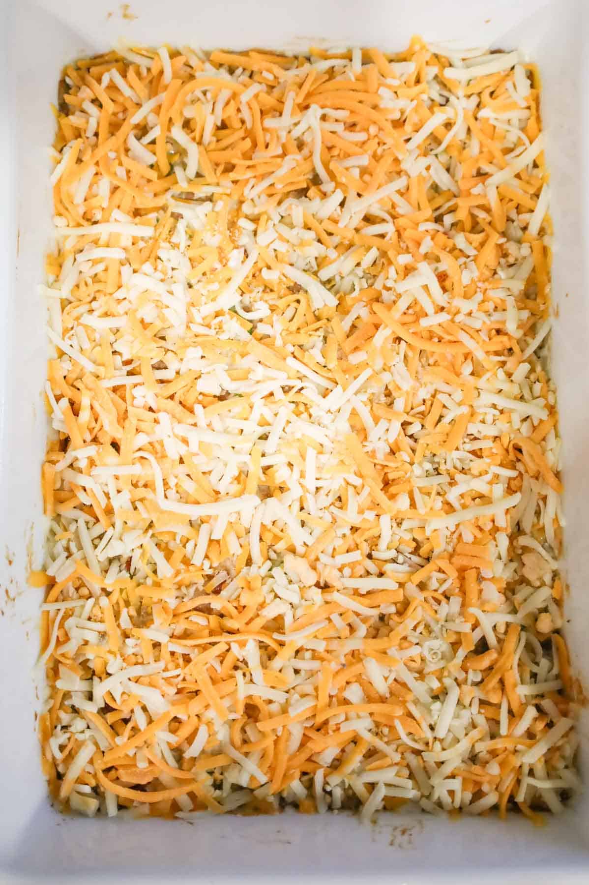 shredded cheese on top of ground beef and rice mixture in a baking dish