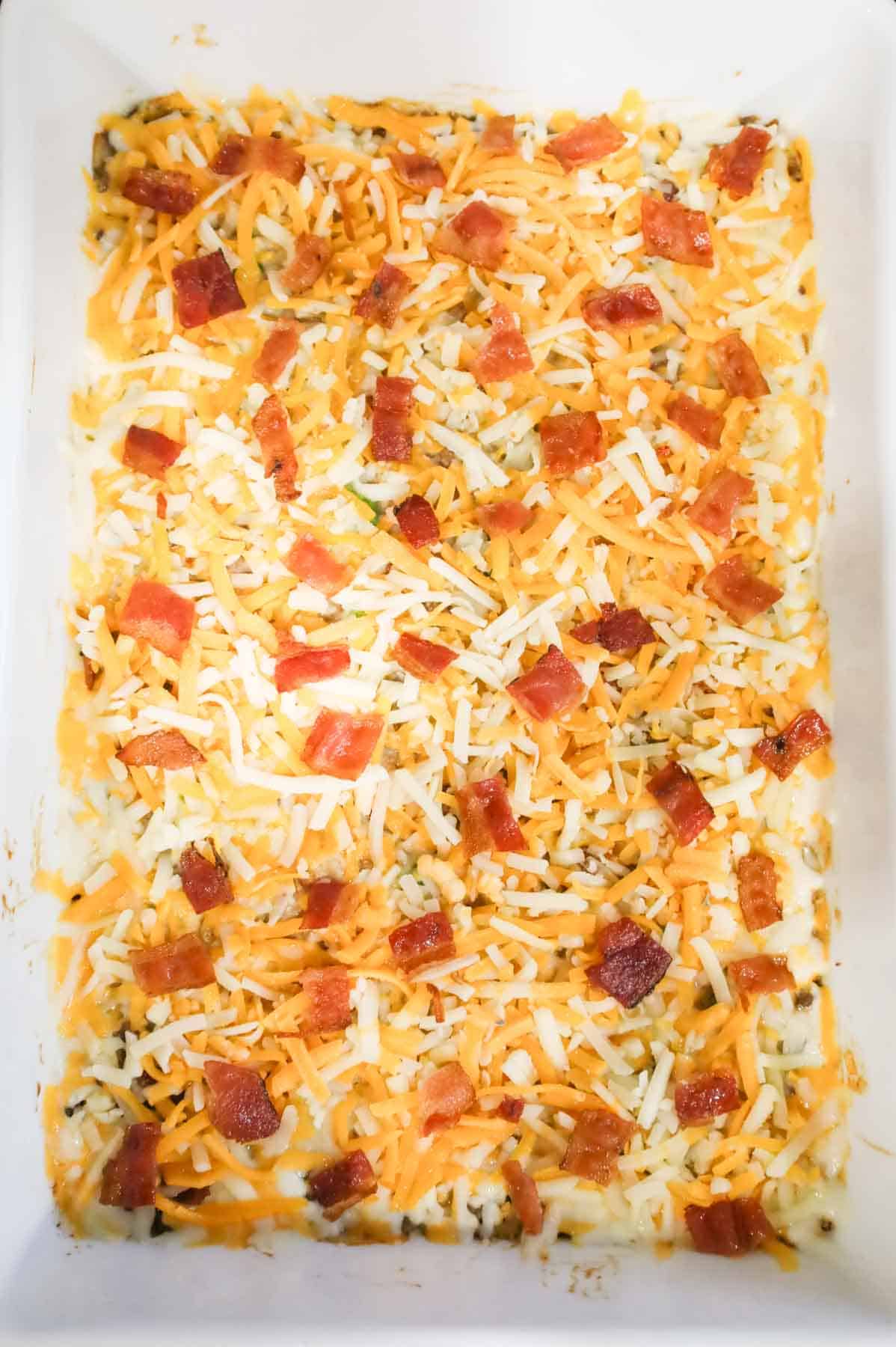 shredded cheese and cooked bacon pieces on top of creamy ground beef and rice mixture in a baking dish