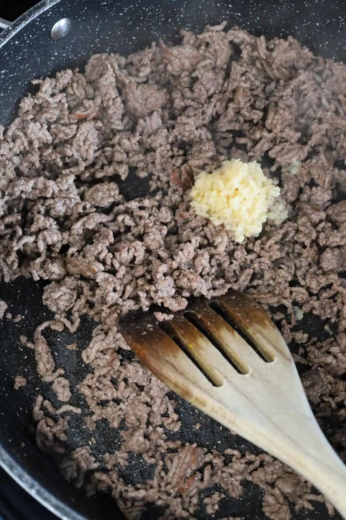 minced garlic on top of cooked ground beef in a skillet