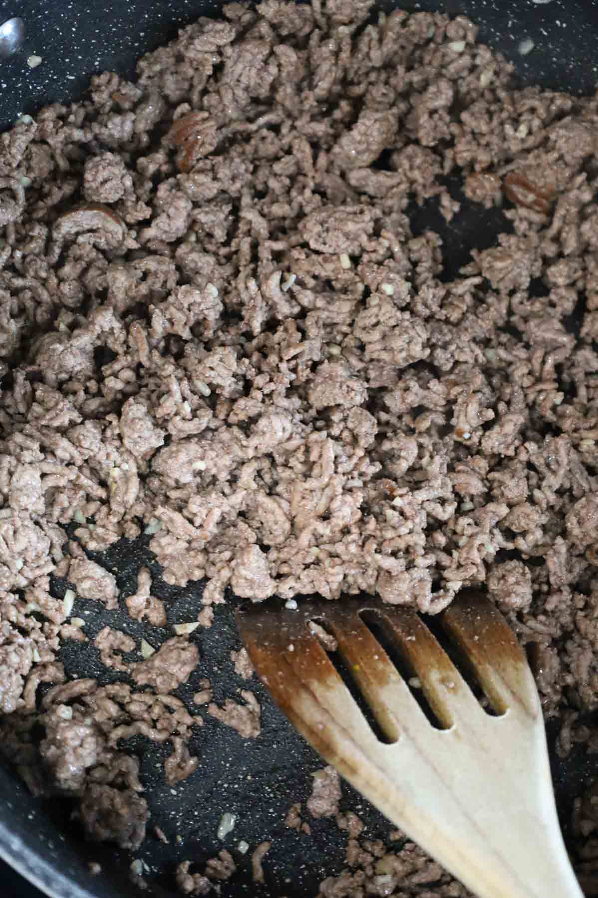 minced garlic being stirred into cooked ground beef