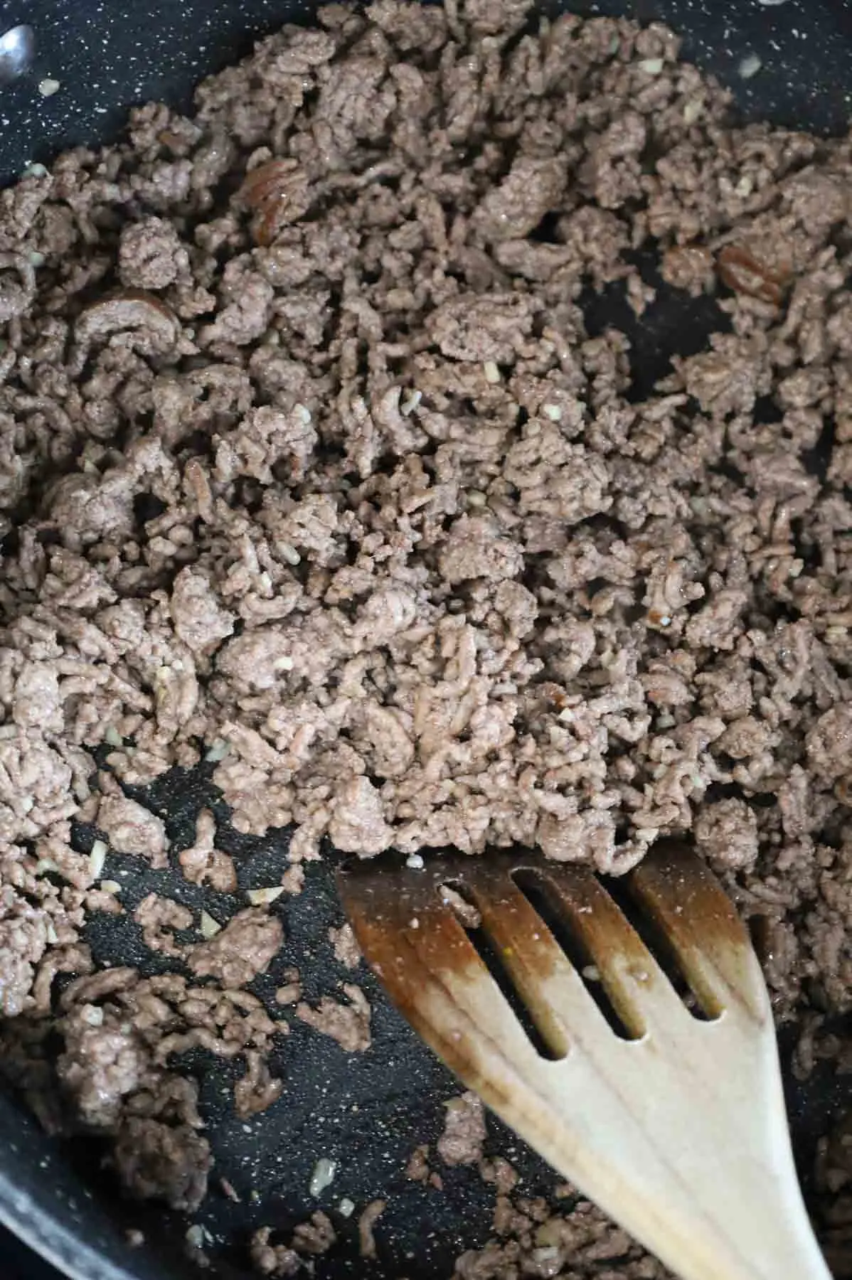 minced garlic being stirred into cooked ground beef