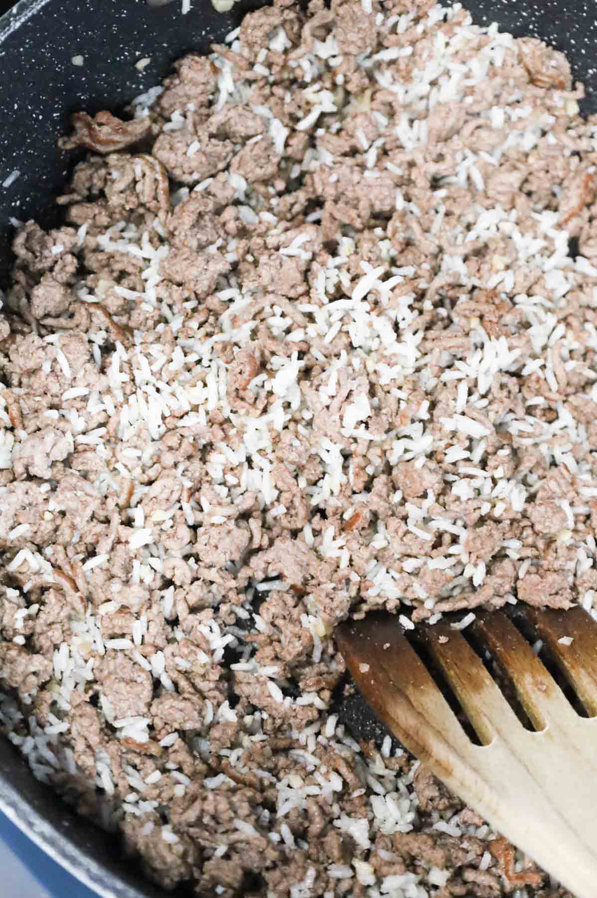 instant rice and ground beef being stirred together in a skillet
