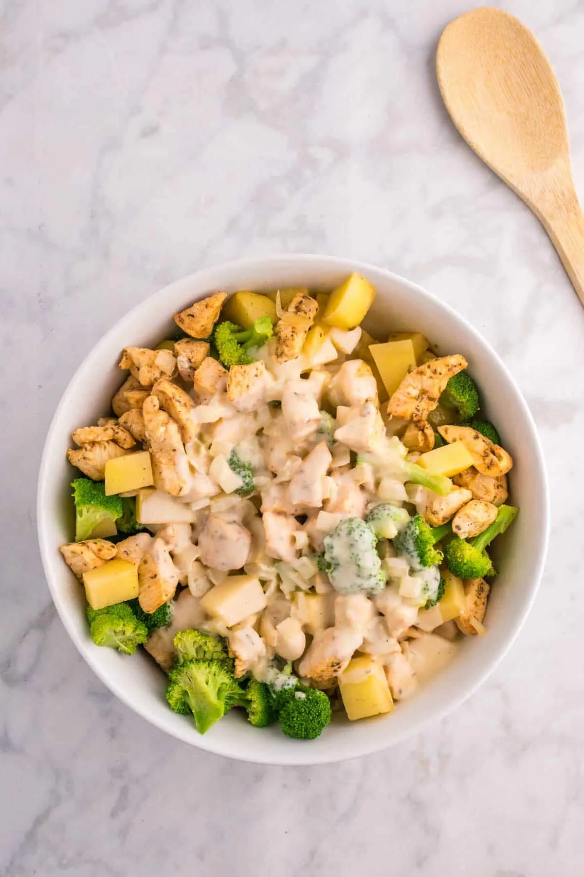 creamy sauce poured over chicken, broccoli and potatoes in a bowl