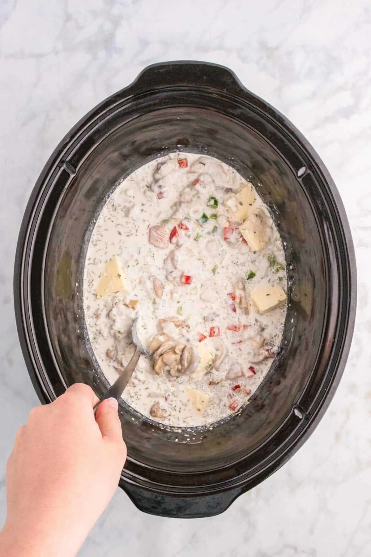 stirring creamy soup mixture with diced veggies and chicken chunks in a Crock Pot