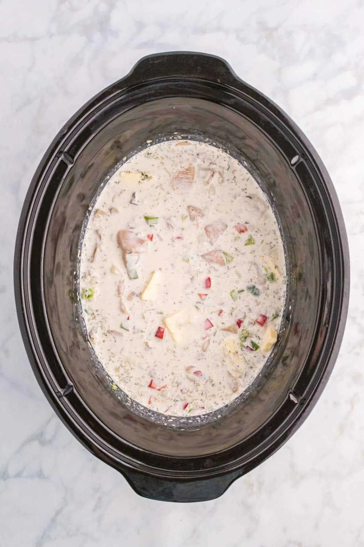 creamy soup mixture poured over chicken and chopped vegetables in a Crock Pot