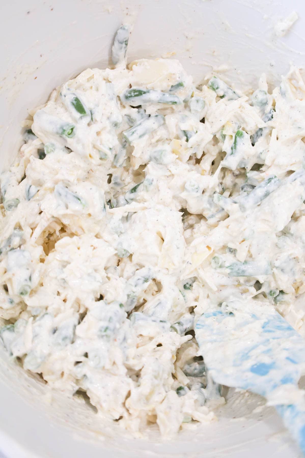shredded cheese, green beans, artichoke hearts, cream cheese and sour cream mixture in a bowl