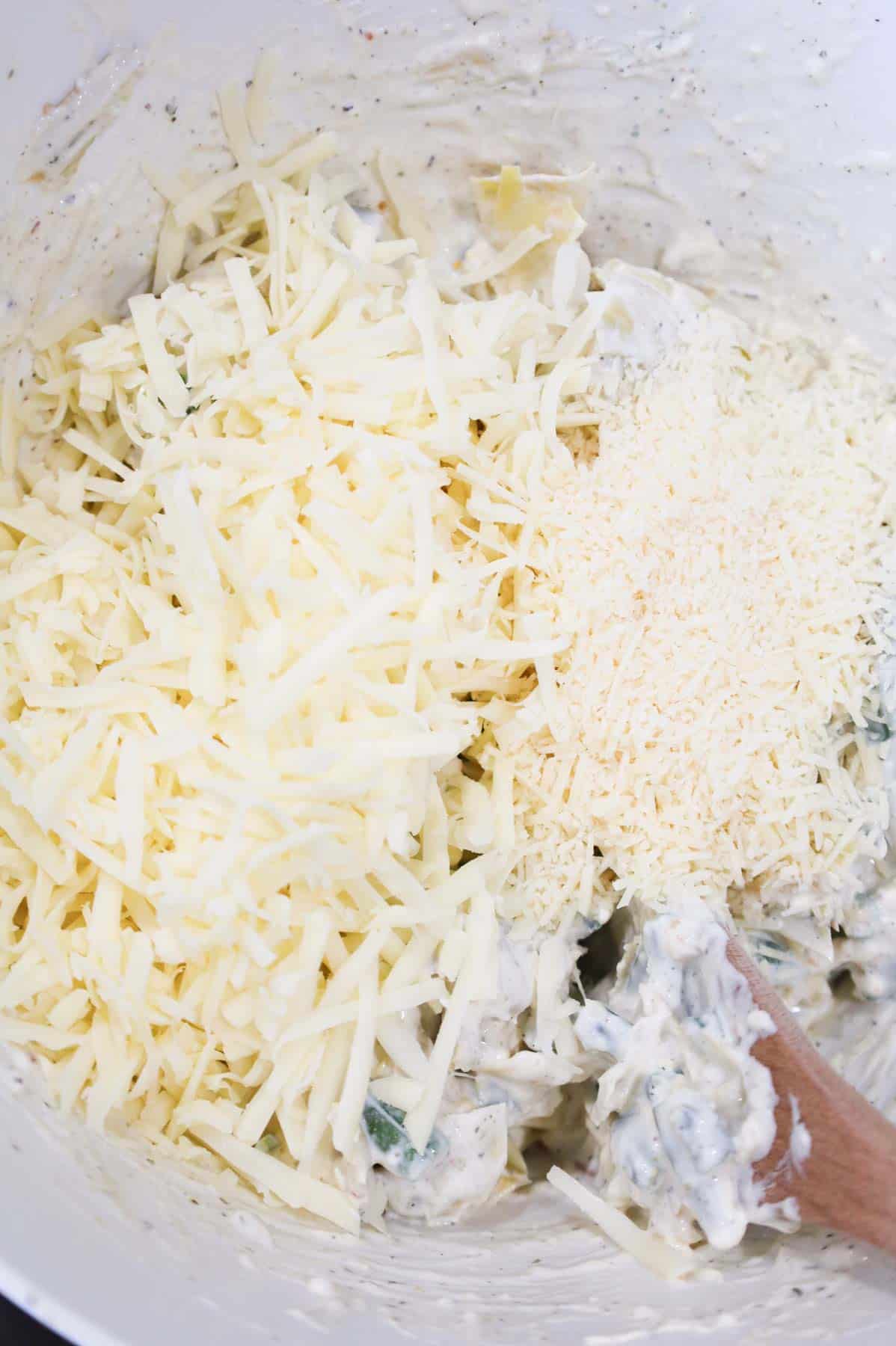 shredded mozzarella and parmesan cheese added to bowl with creamy green bean and artichoke mixture