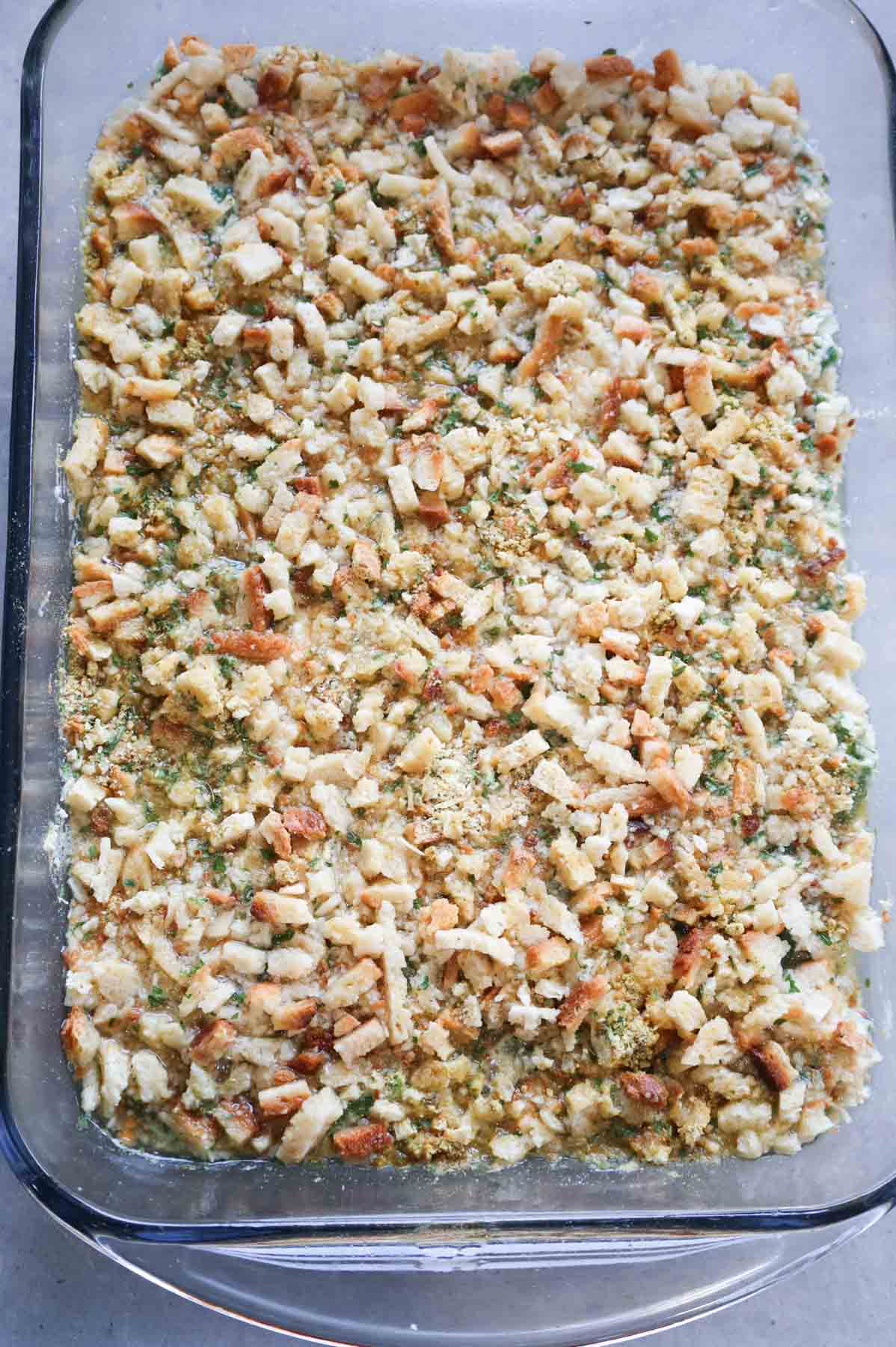 stove top stuffing mix soaked in chicken broth on top of green bean casserole in a baking dish