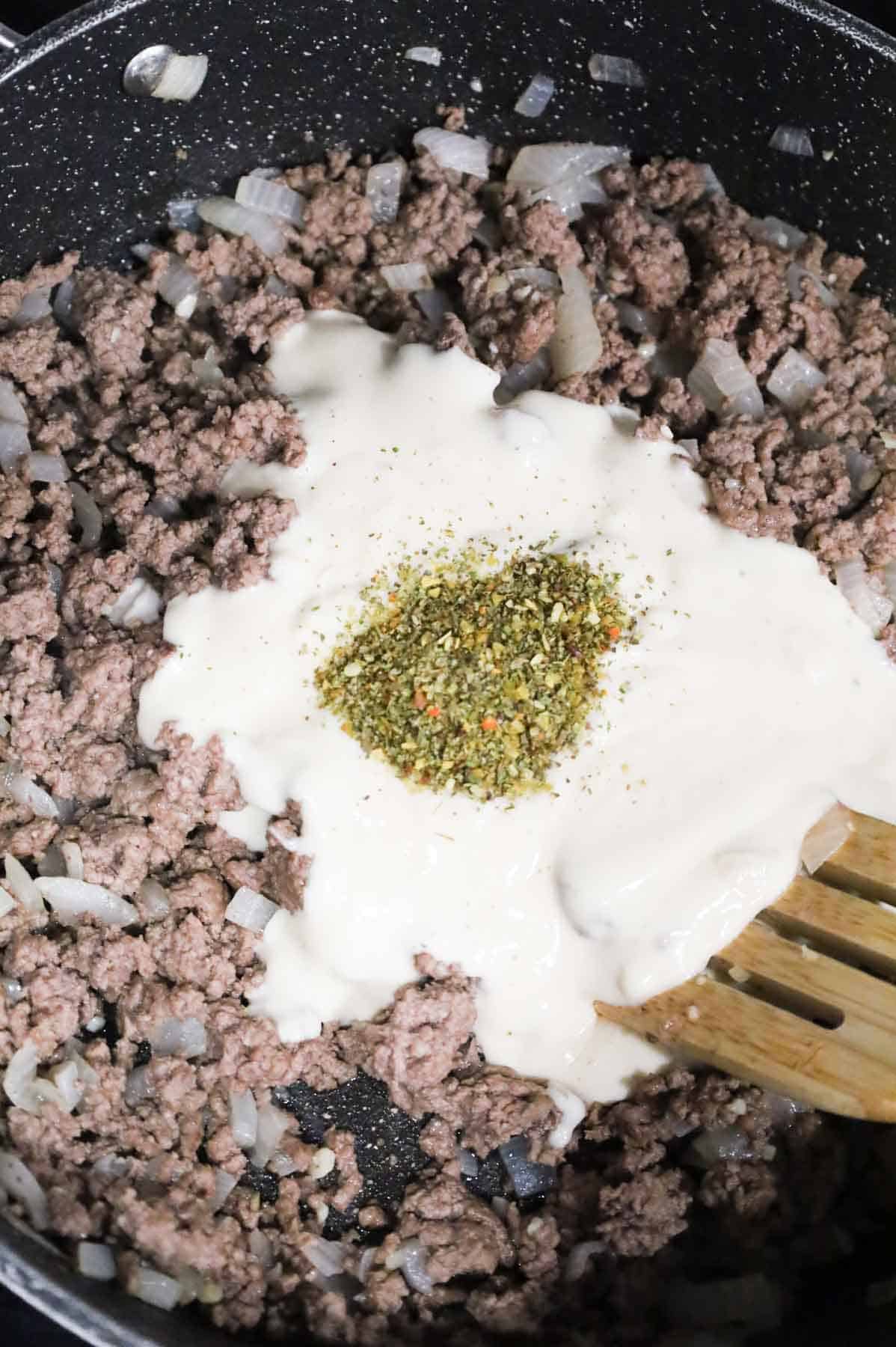 Italian seasoning and alfredo sauce on top of cooked ground beef in a skillet