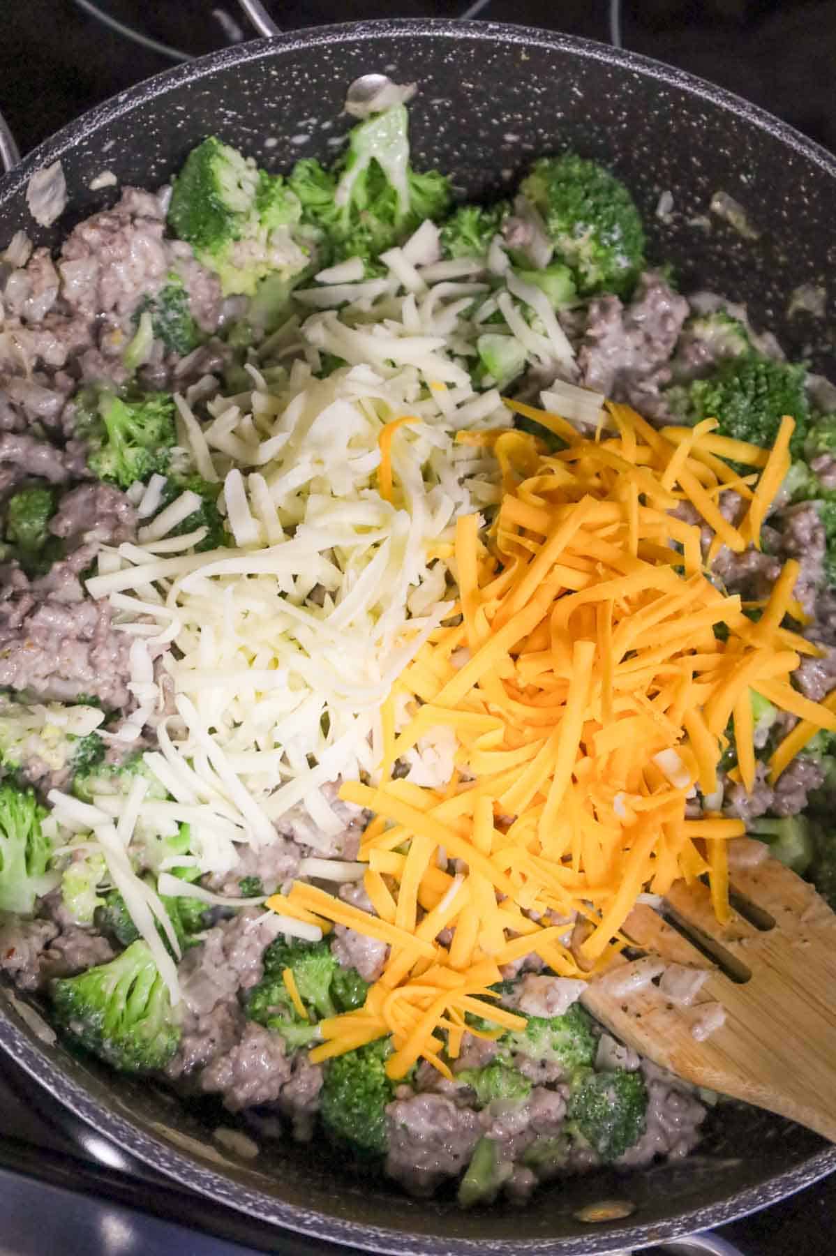 shredded mozzarella and shredded cheddar cheese on top of ground beef and broccoli mixture in a skillet
