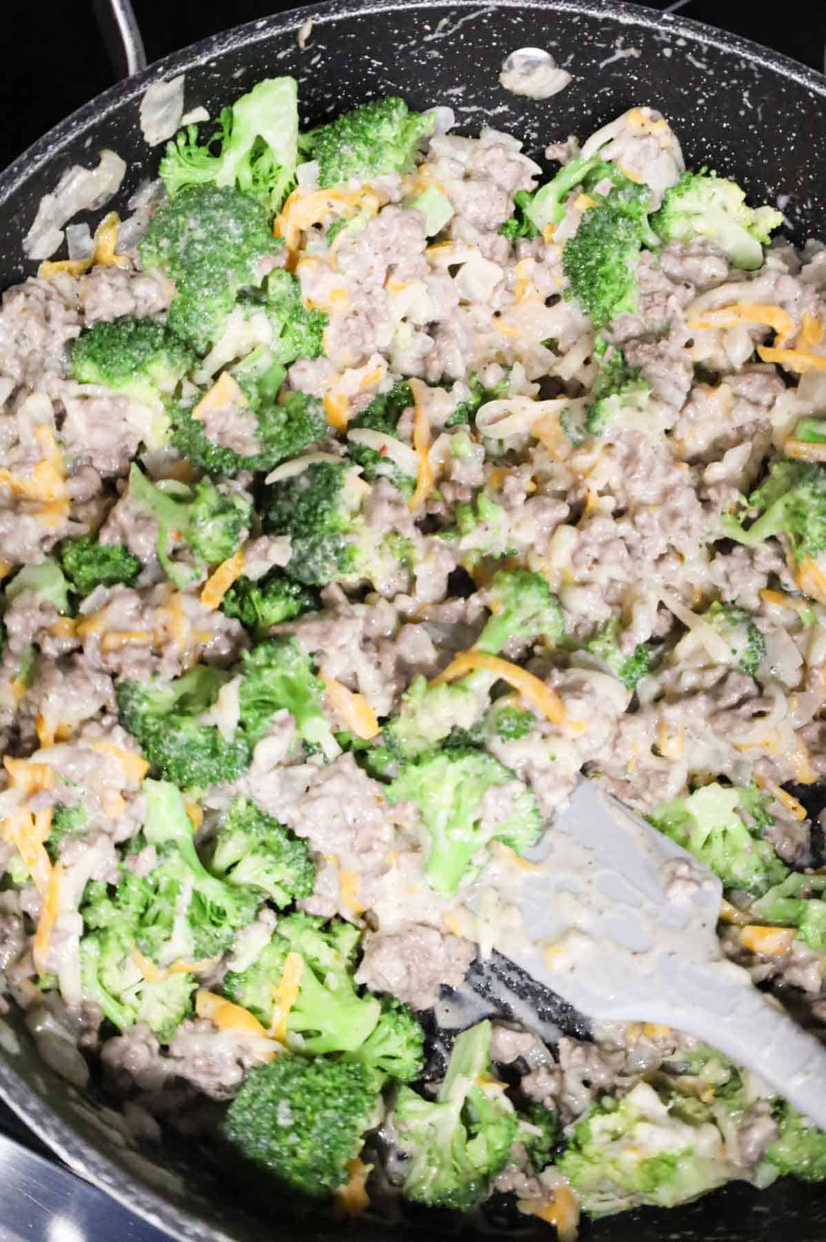 broccoli, shredded cheese and ground beef mixture being stirred in a skillet