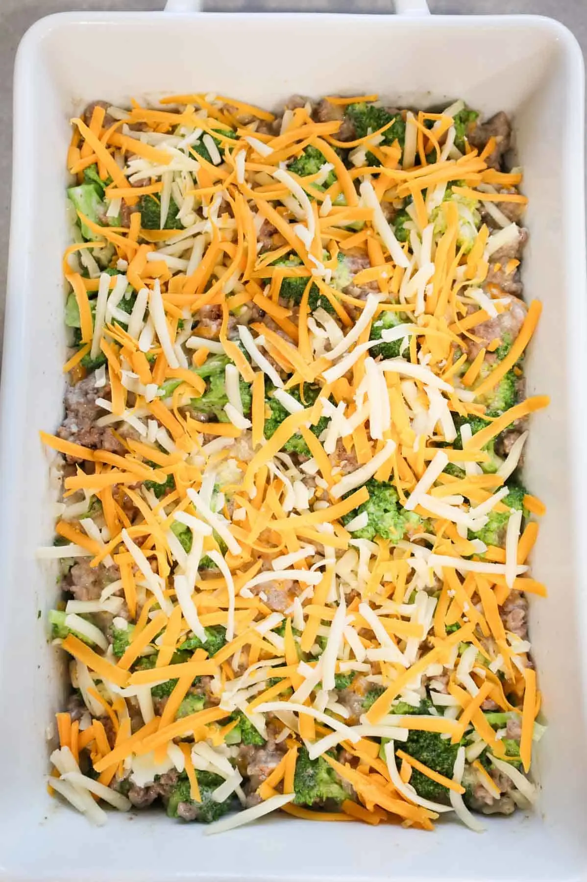 shredded mozzarella and shredded cheddar on top of ground beef and broccoli mixture in casserole dish