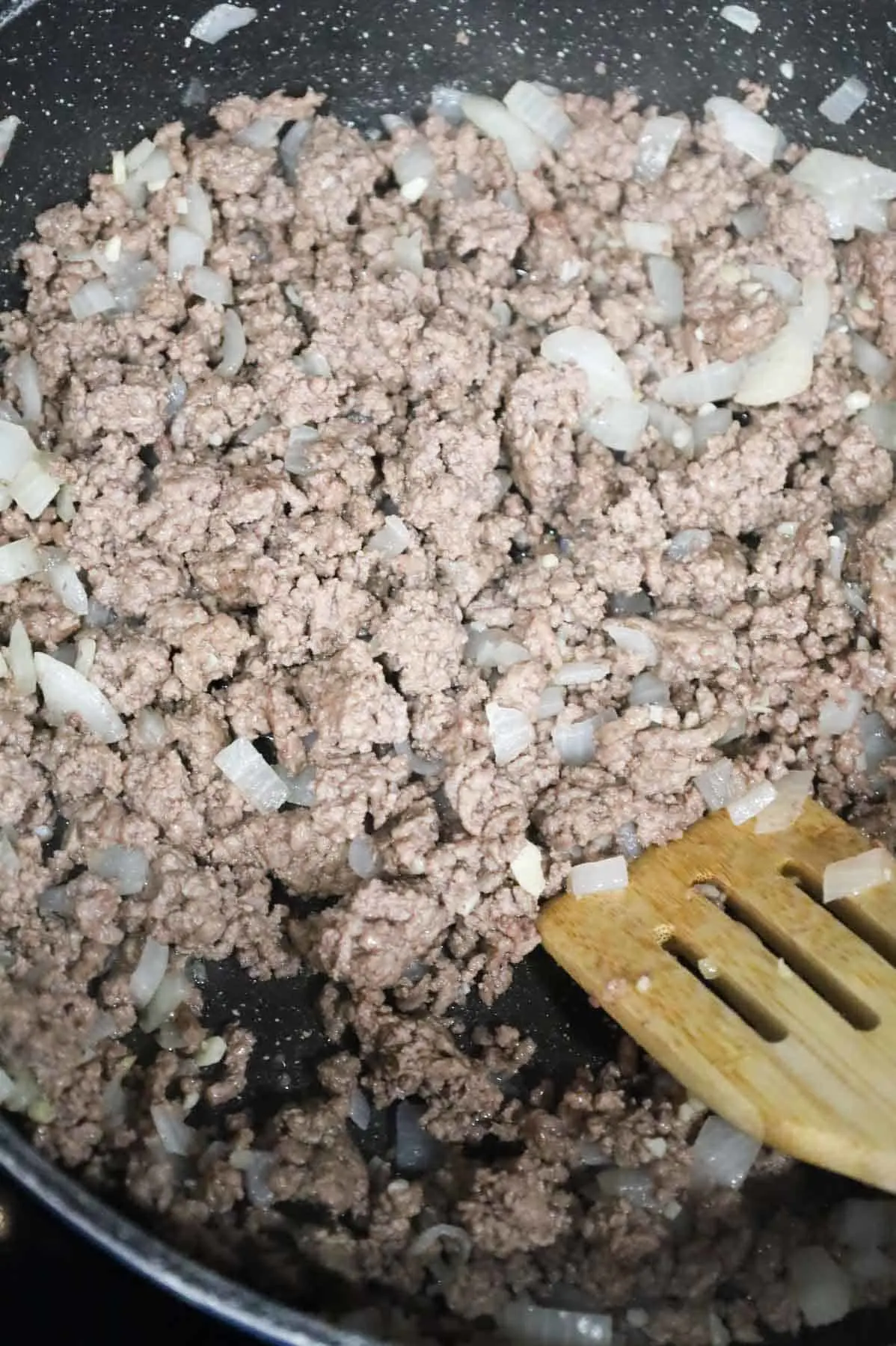 minced garlic being stirred into cooked ground beef and onions in a skillet