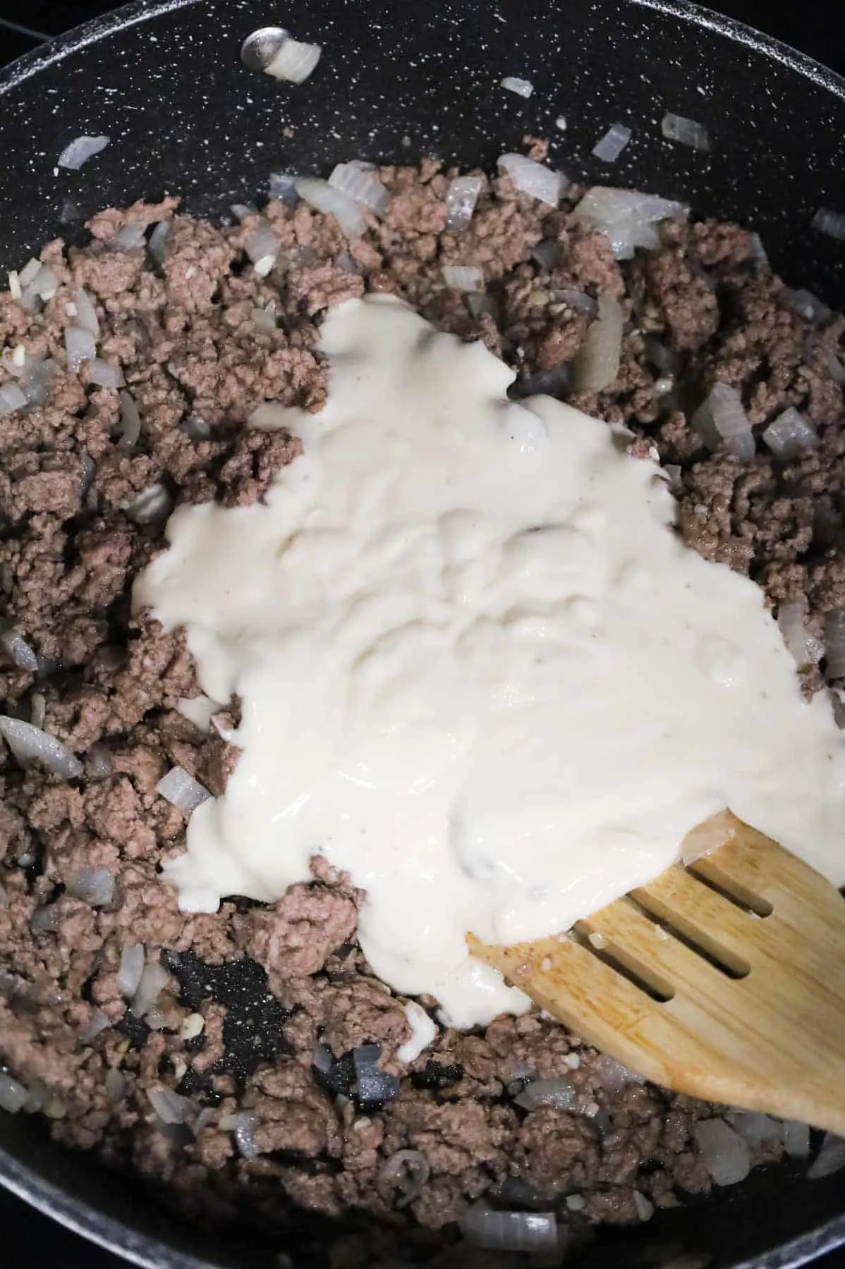 alfredo sauce poured over cooked ground beef and onions in a skillet