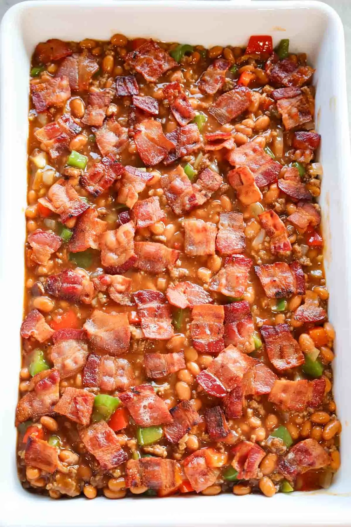 cooked bacon pieces on top of ground beef, bell pepper and bean mixture in a baking dish