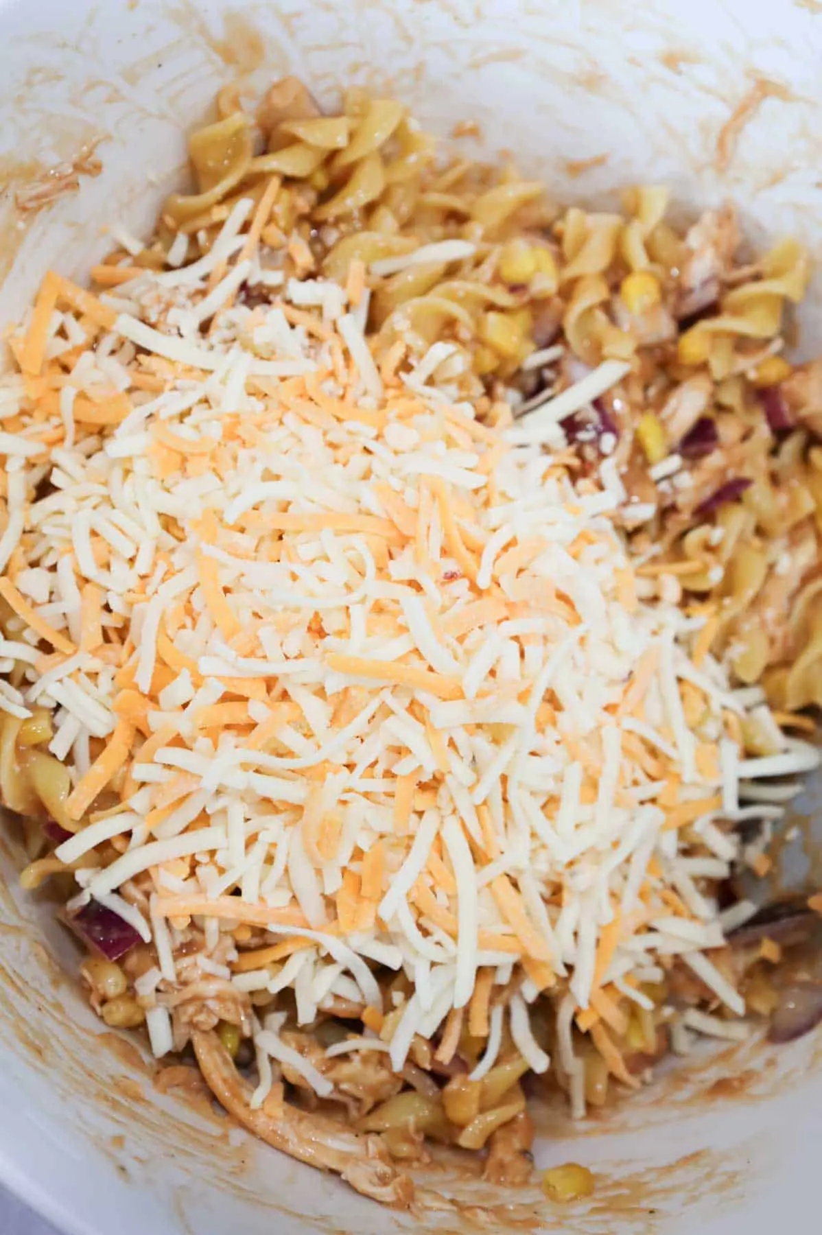 shredded cheddar cheese on top of bbq chicken and noodle mixture in a bowl