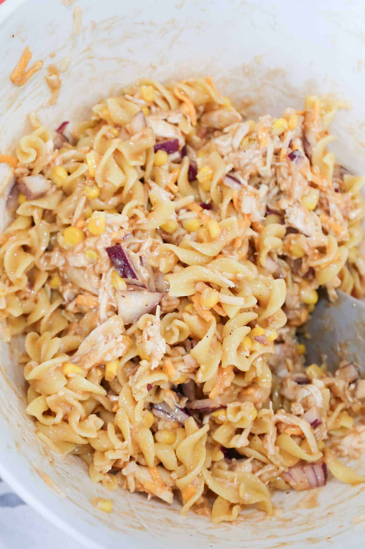 shredded cheese being stirred into barbecue chicken and egg mixture in a bowl