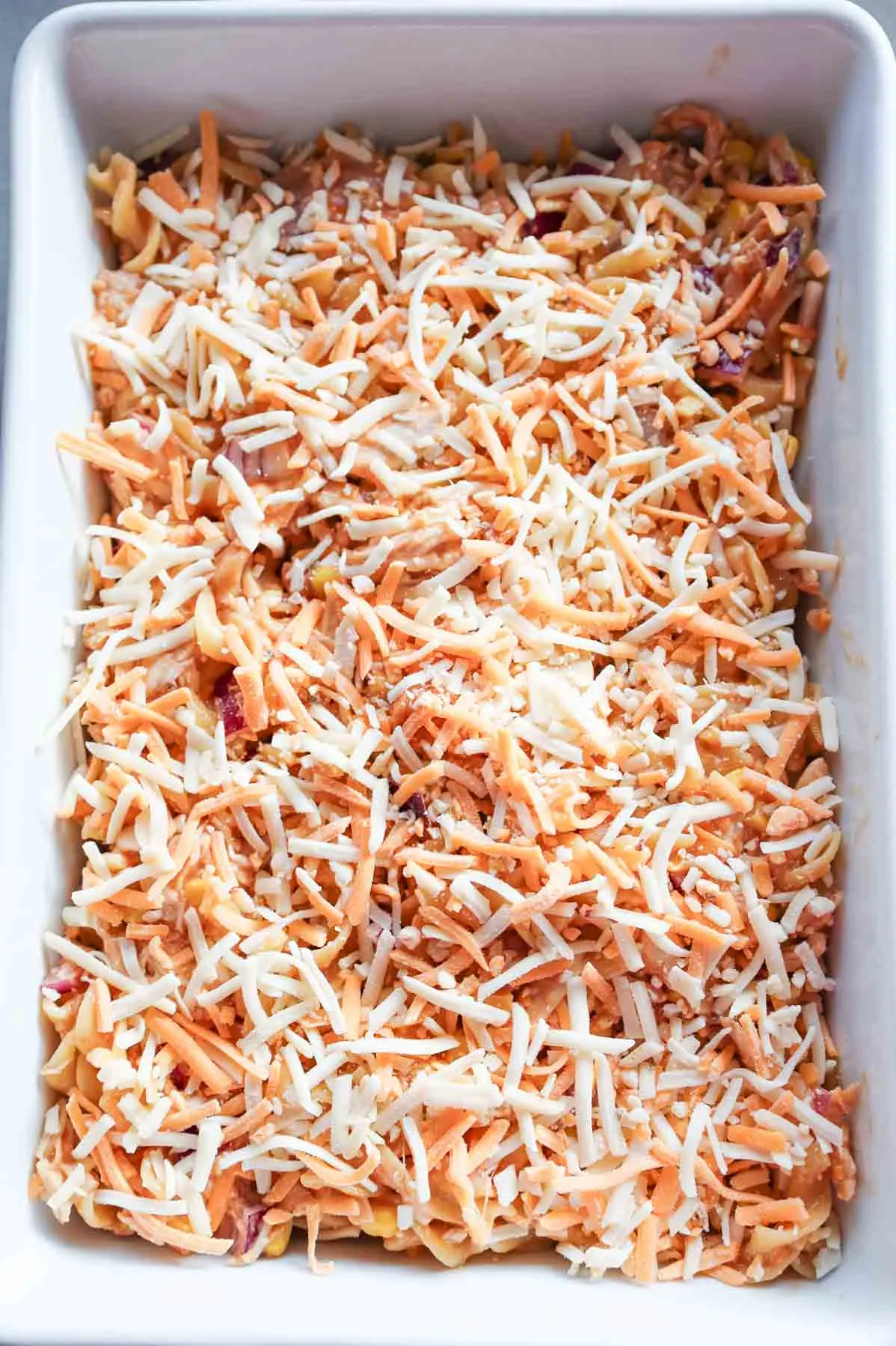 shredded cheese on top of barbecue chicken and egg noodle mixture in a baking dish