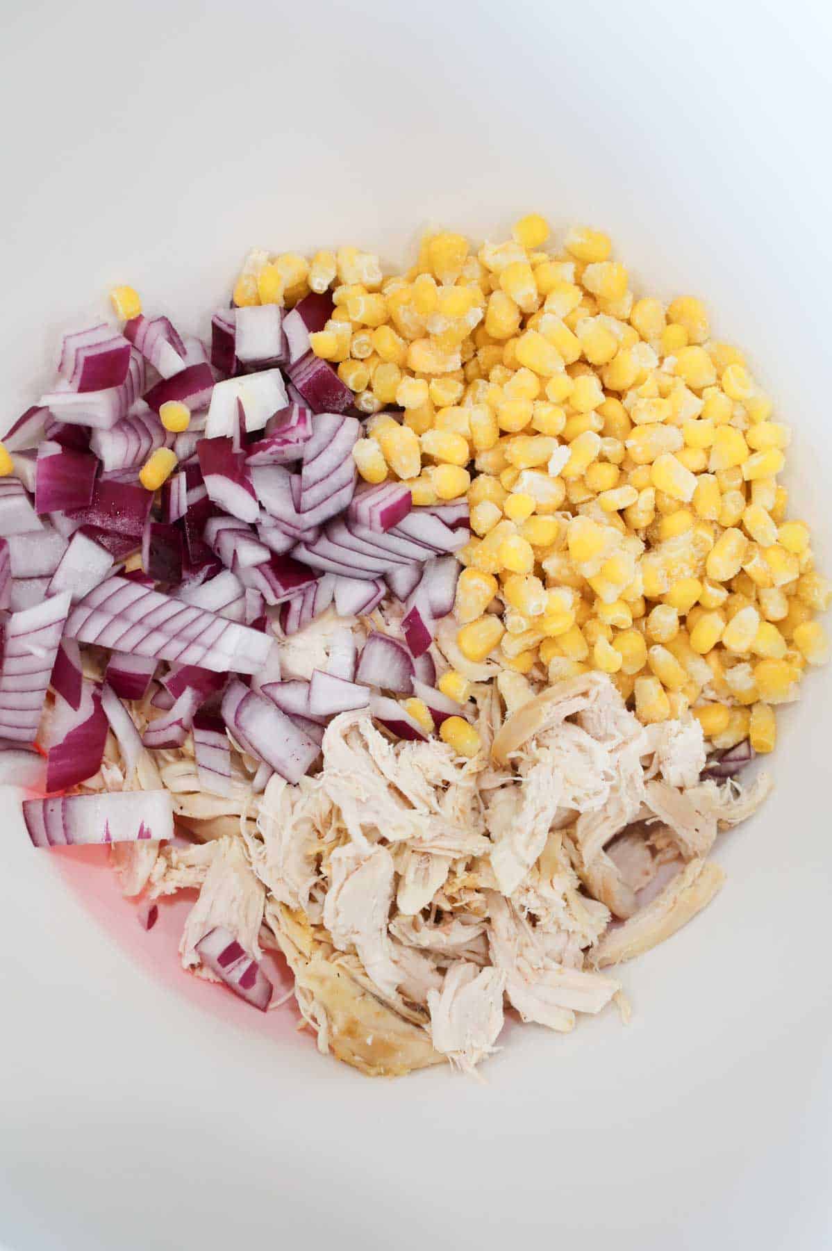 corn kernels, diced red onions and shredded chicken in a bowl