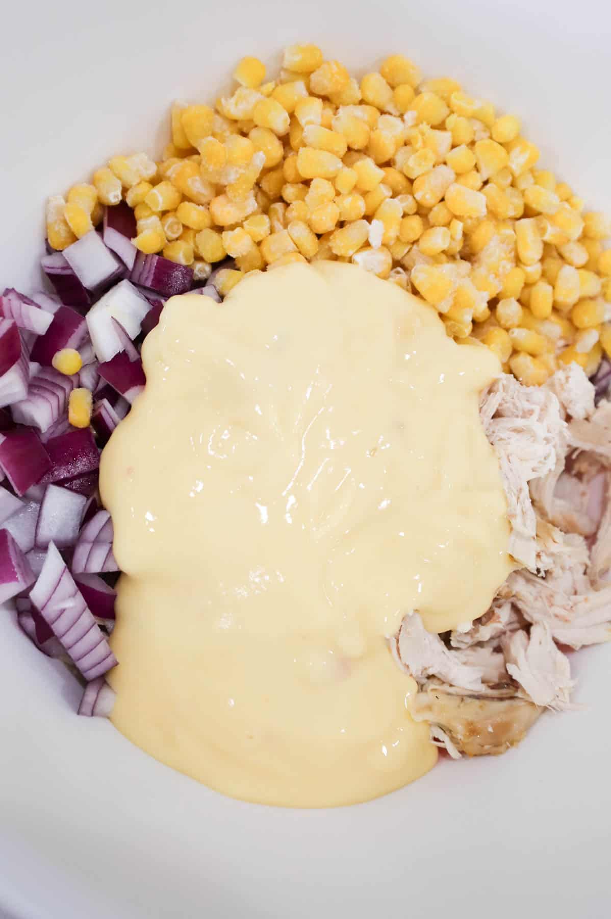 cream of chicken soup on top of diced red onions, corn and shredded chicken in a bowl