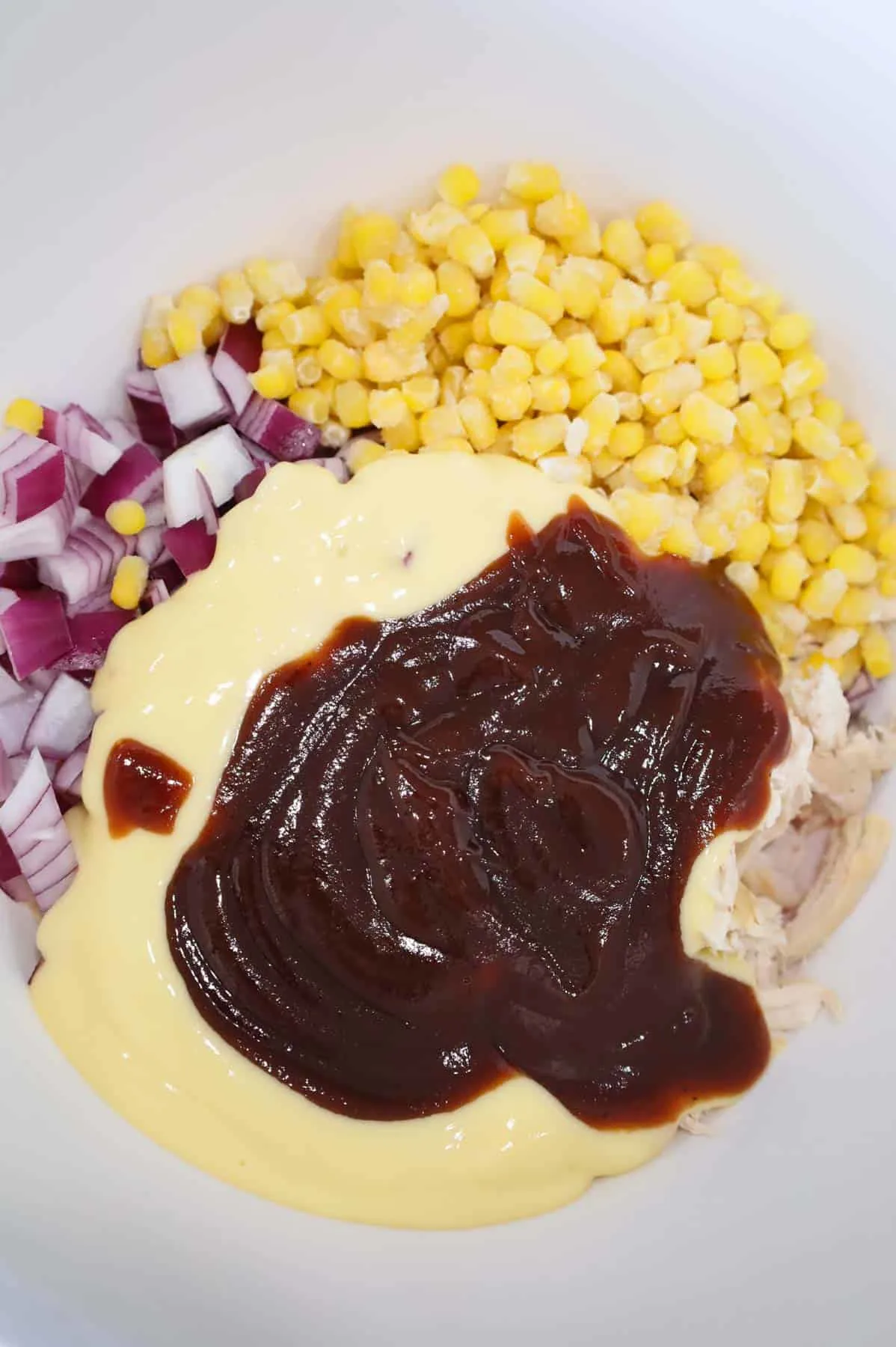 barbecue sauce, cream of chicken soup, diced red onions, corn and shredded chicken in a bowl
