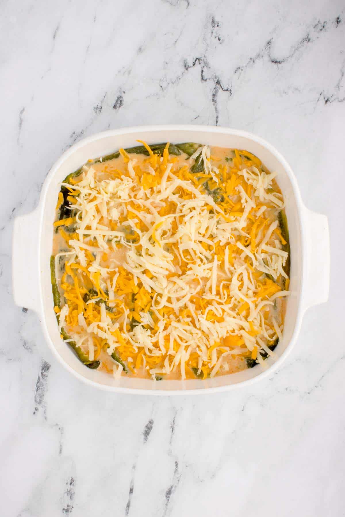 shredded cheese on top of egg batter in a baking dish