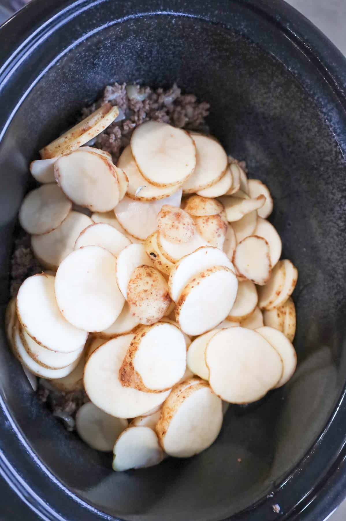 sliced potatoes on top of cooked ground beef in a slow cooker