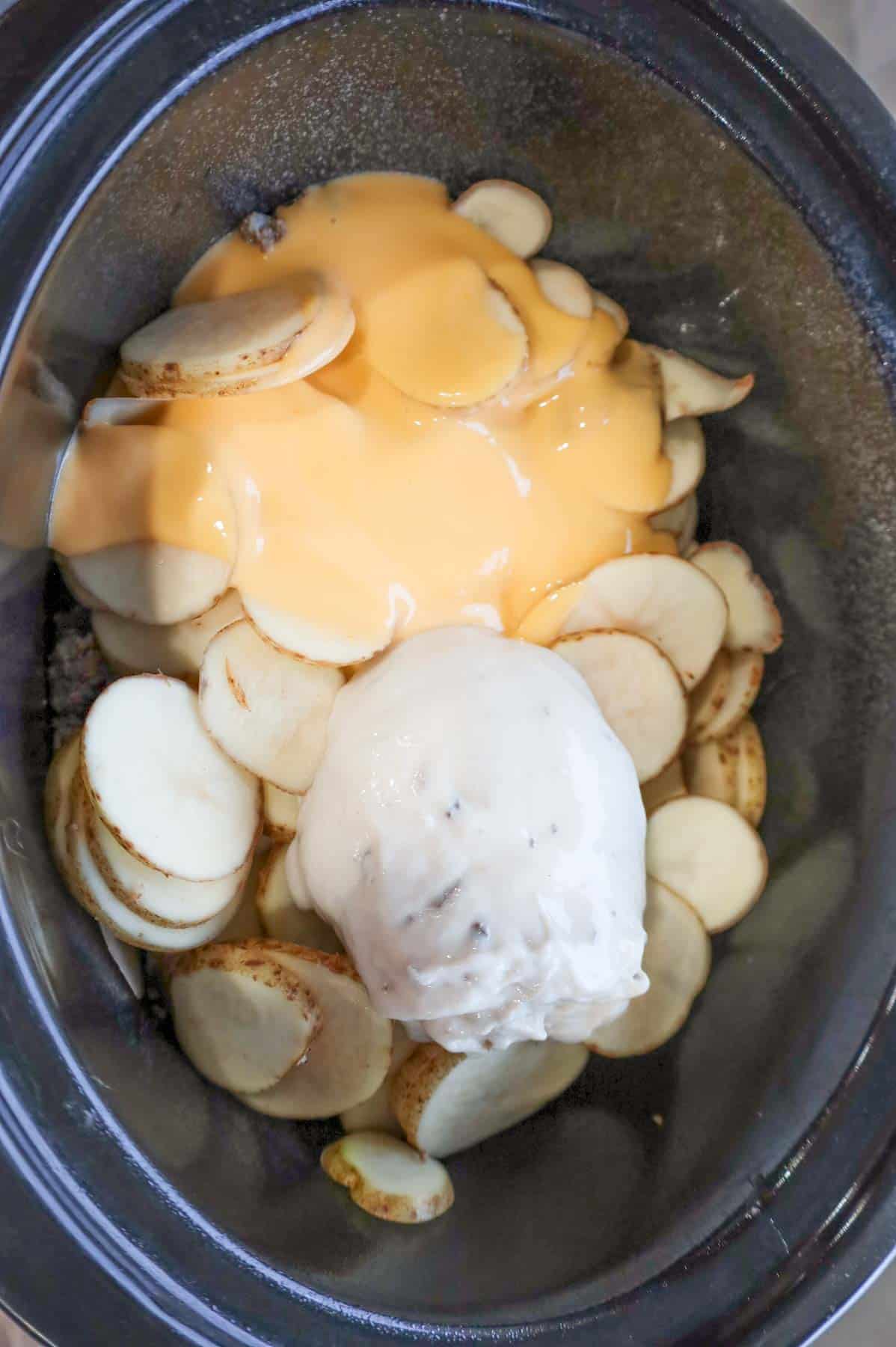 cheddar soup and cream of mushroom soup poured over sliced potatoes in a slow cooker