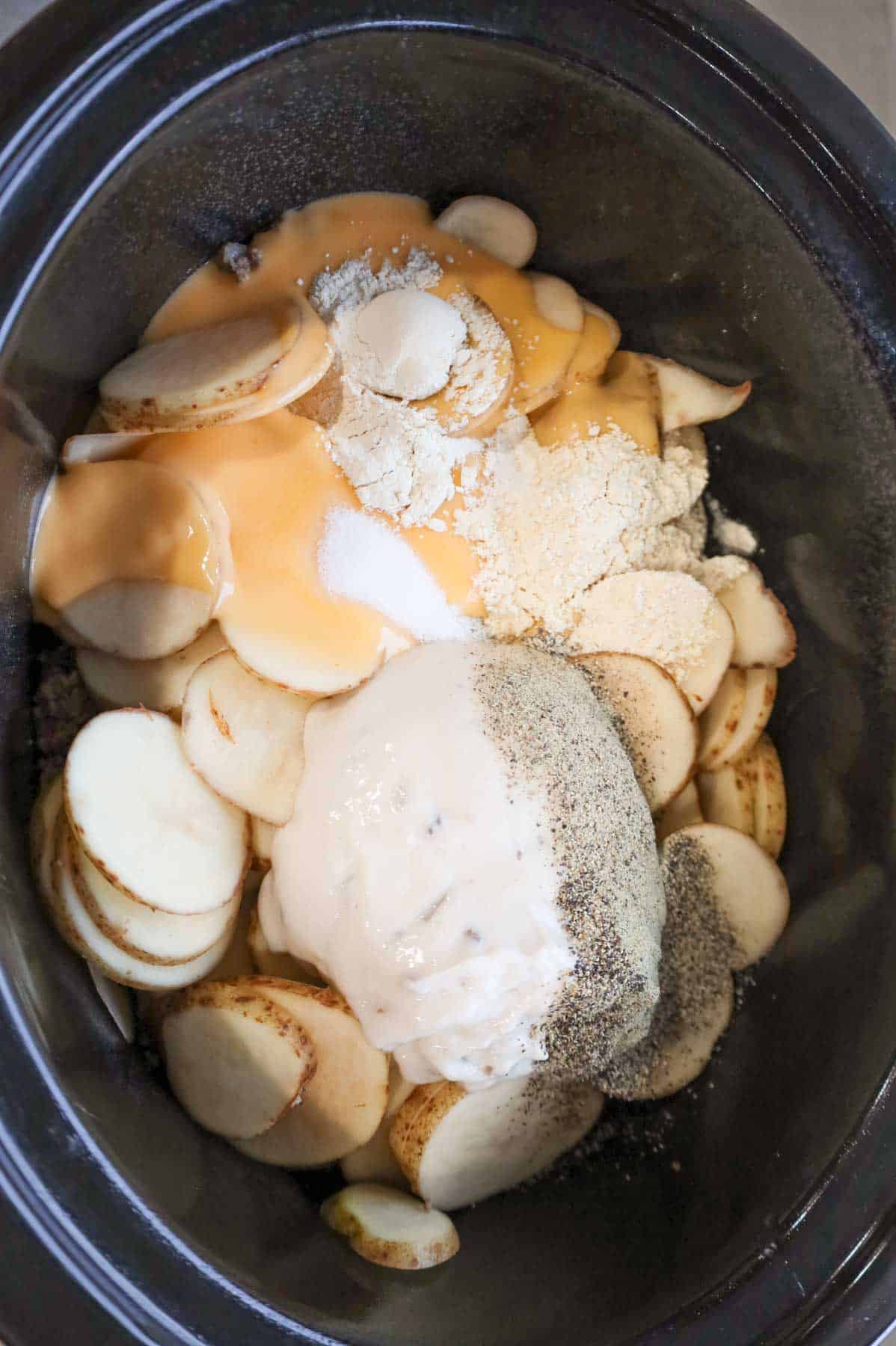 spices, cheddar soup and cream of mushroom soup on top of sliced potatoes in a Crock Pot