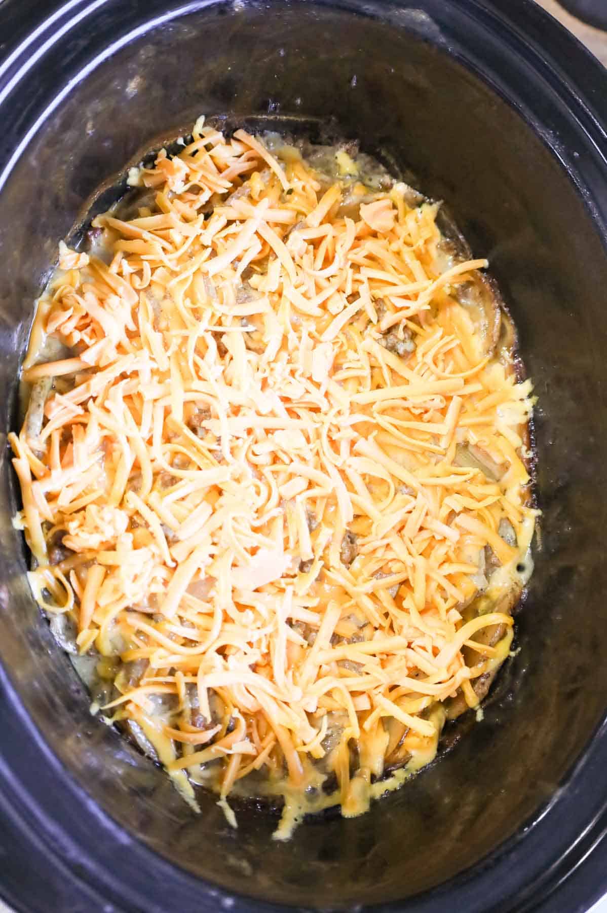 shredded cheddar cheese on top of hamburger potato casserole in a slow cooker