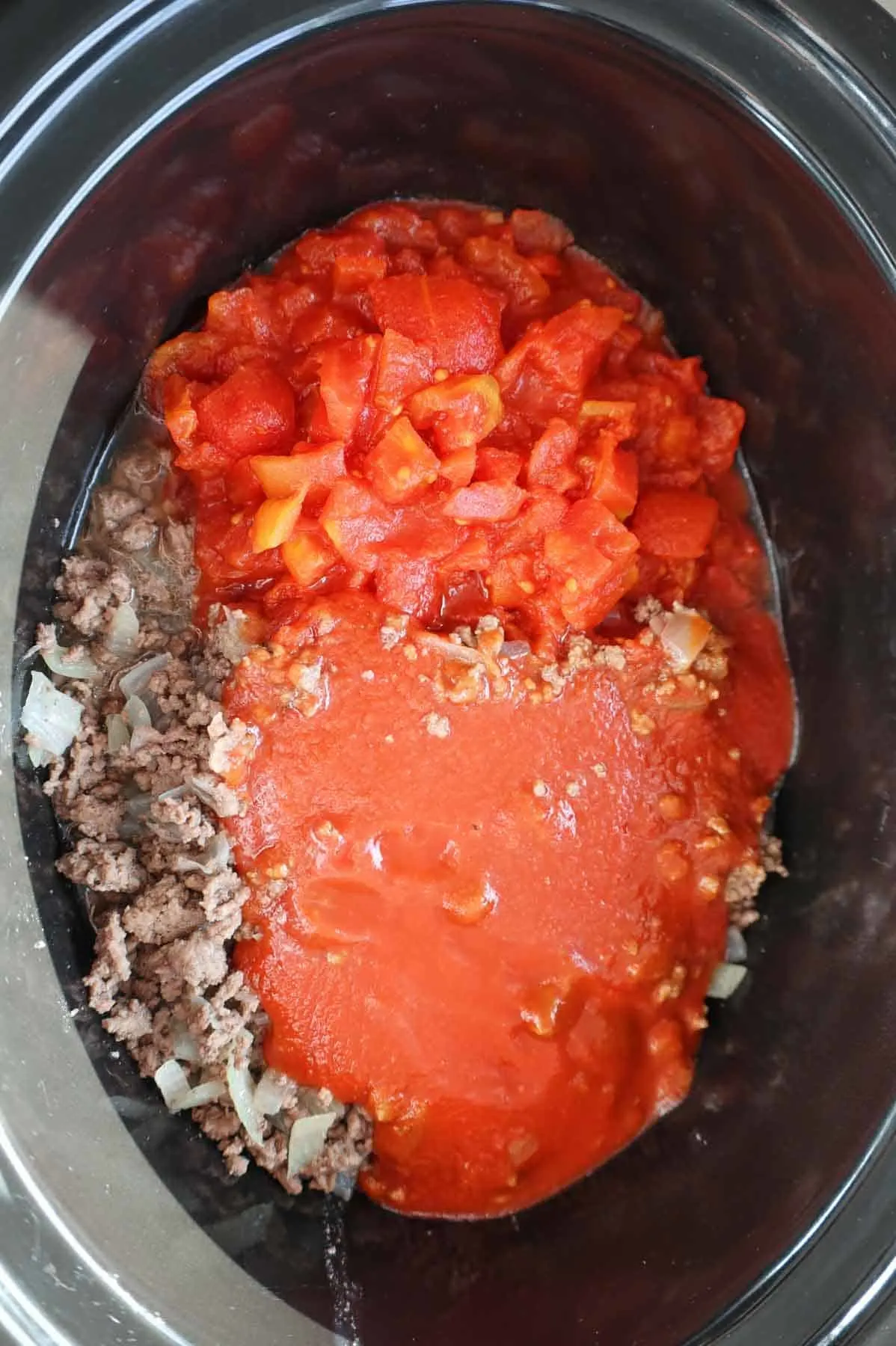 diced tomatoes and tomato sauce on top of cooked ground beef in a slow cooker