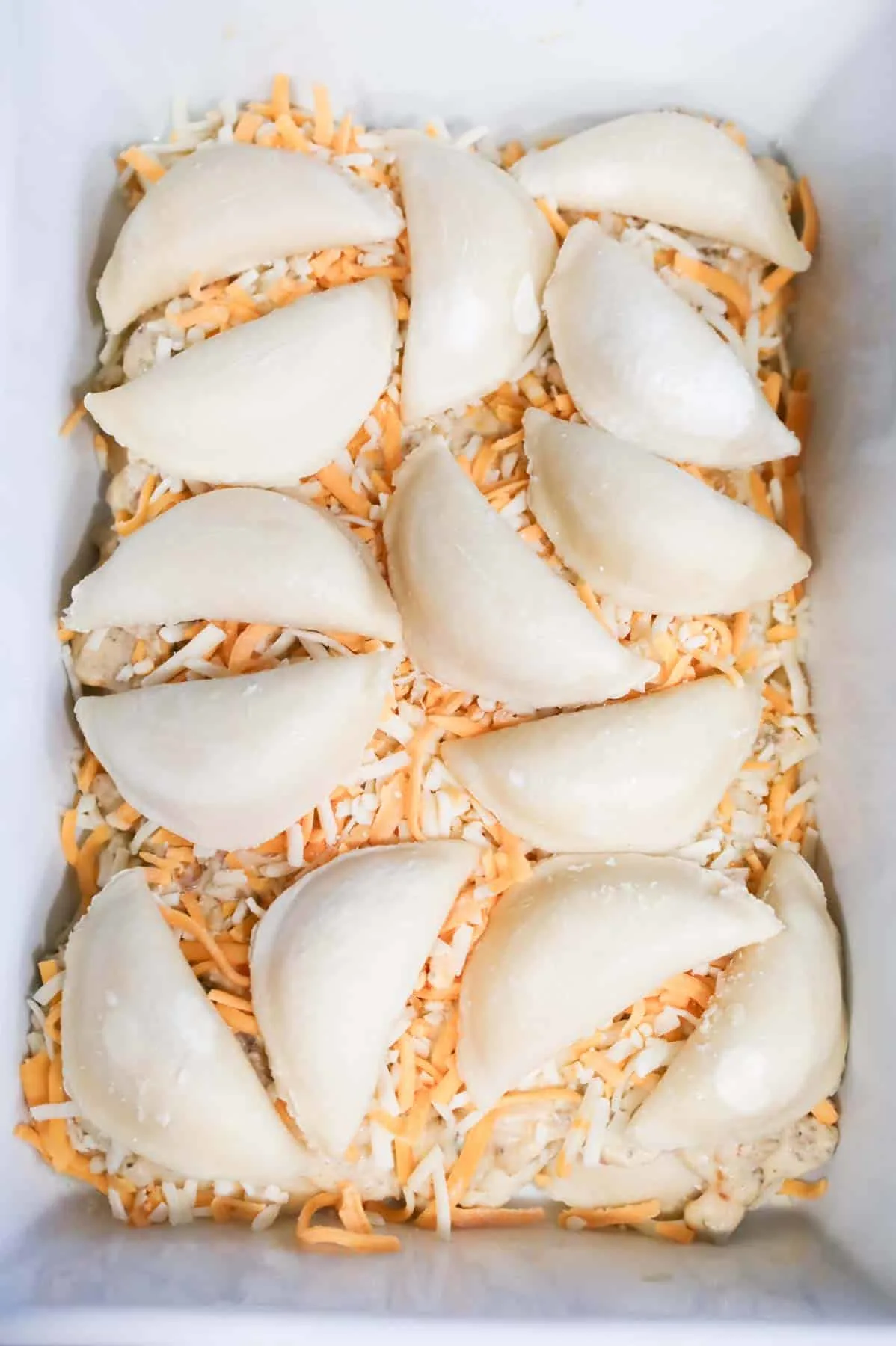 frozen pierogies on top of shredded cheese in a baking dish