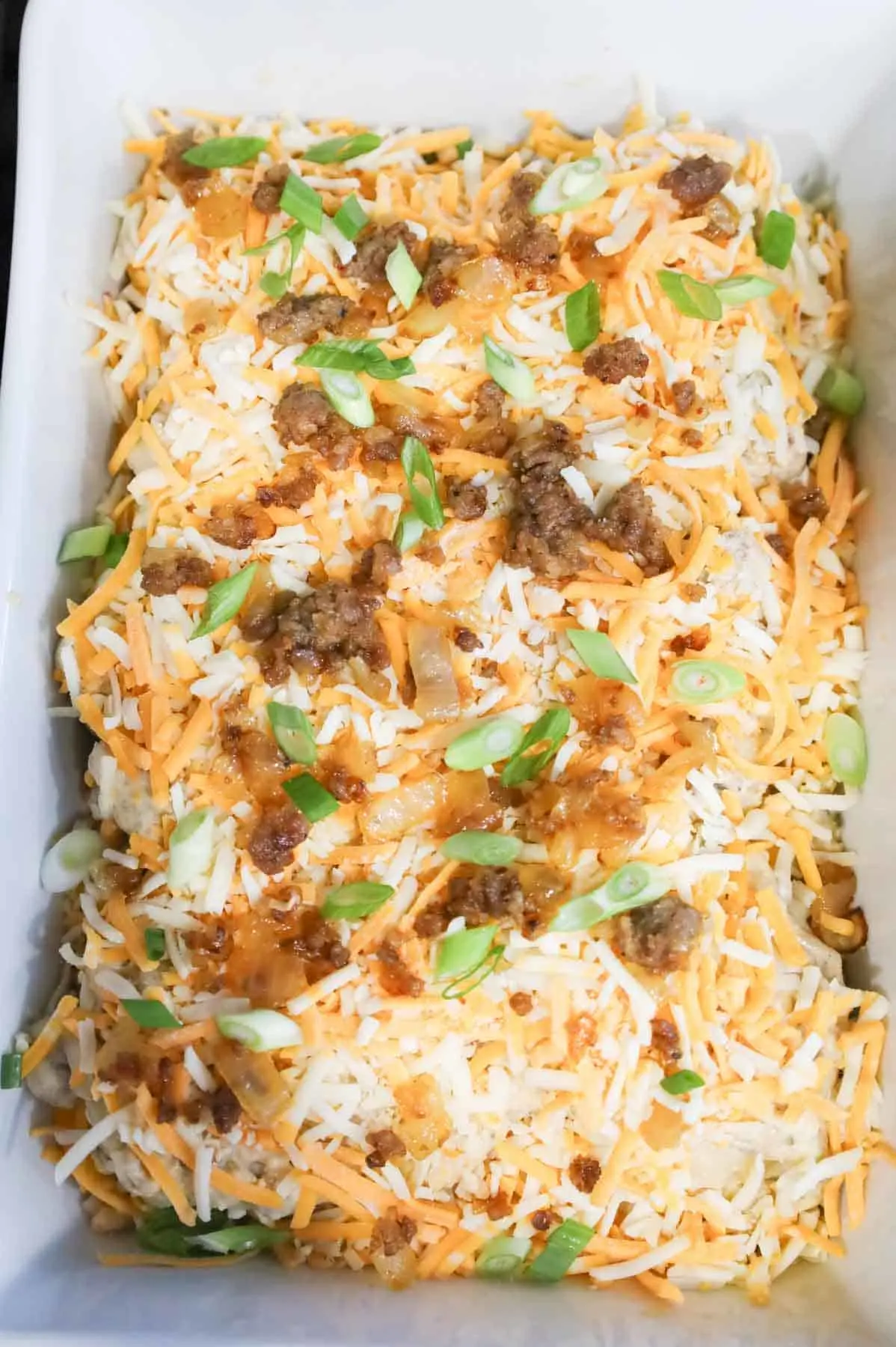 crumbled sausage, green onions and shredded cheese on top of pierogies in a baking dish