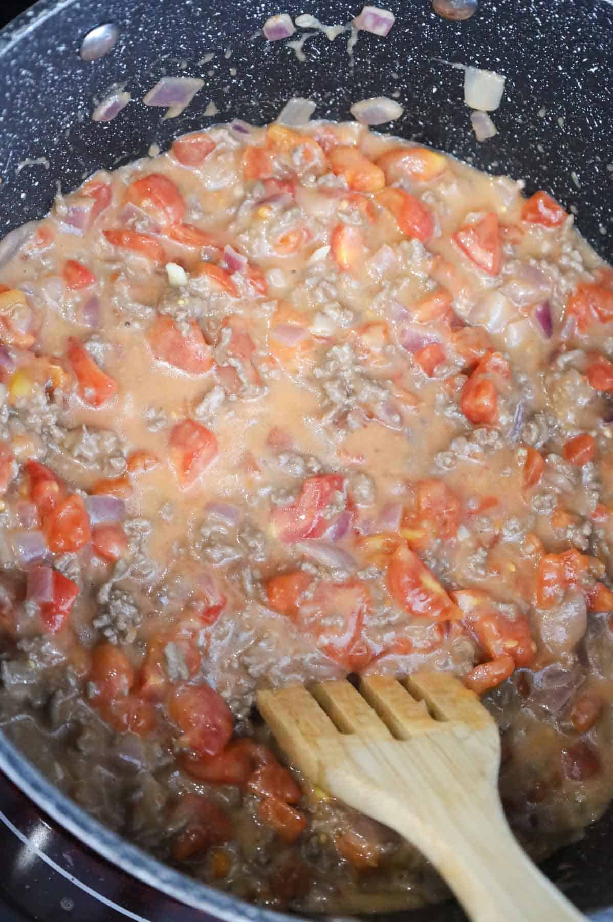 cheddar soup and diced tomatoes being stirred with ground beef in apot