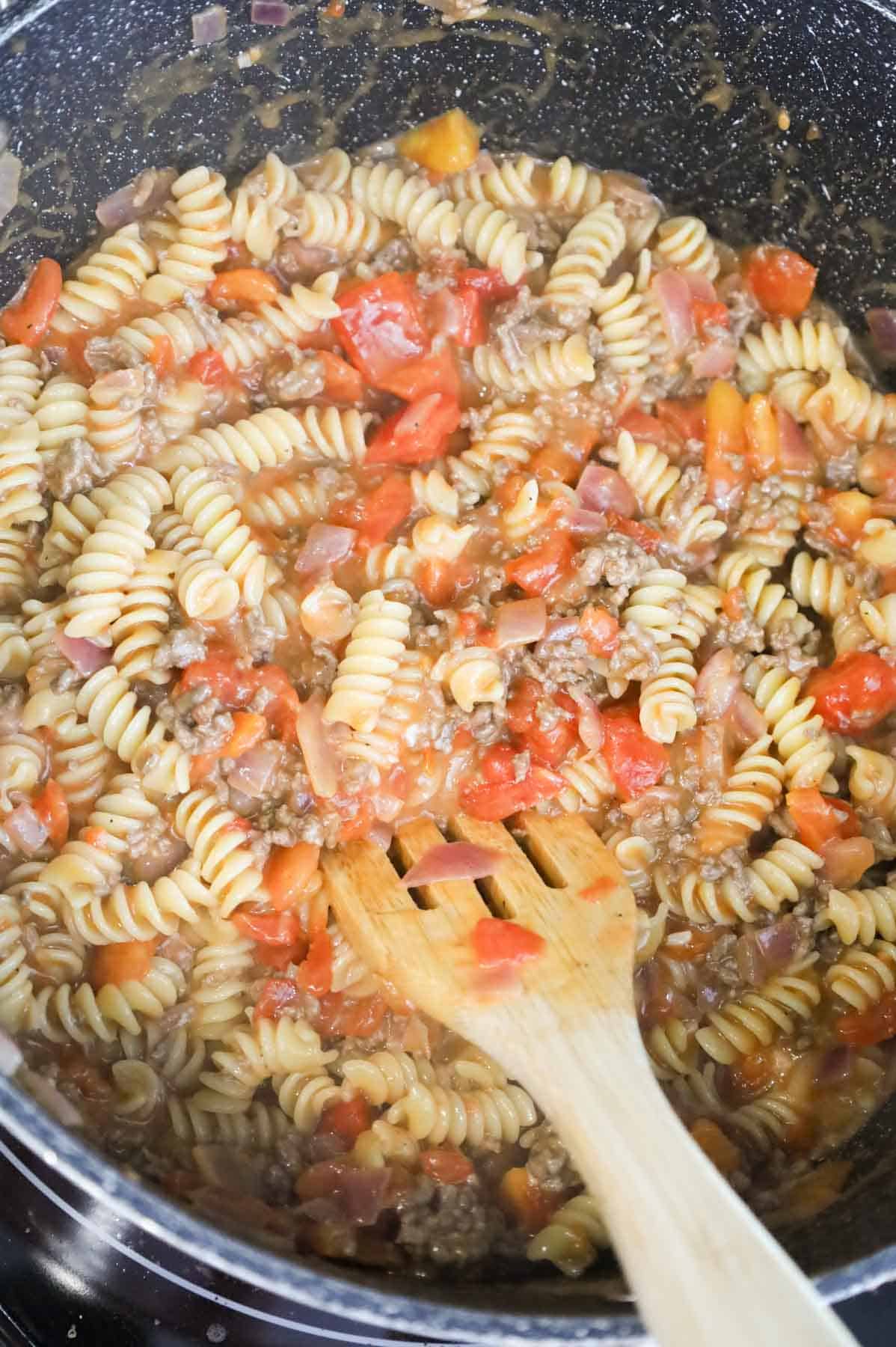 stirring rotini into ground beef mixture in a pot