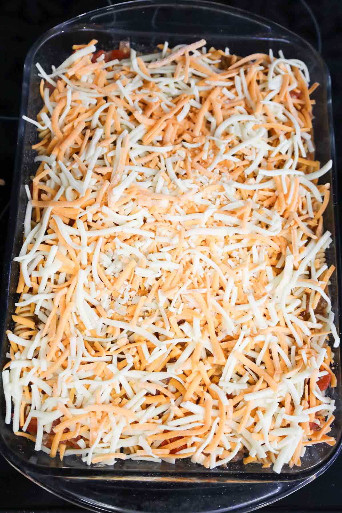 shredded cheddar cheese on top of ground beef pasta mixture in a baking dish