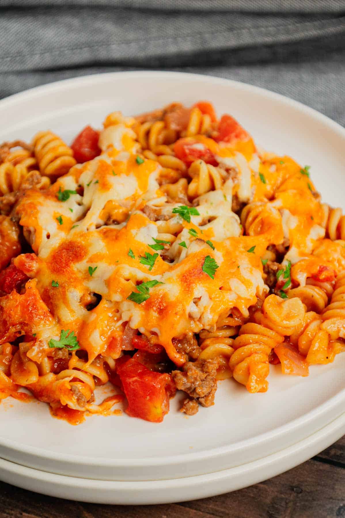 Cheeseburger Casserole is a hearty dish loaded with rotini pasta, ground beef, diced red onions, diced tomatoes, cheddar soup and shredded cheddar cheese.