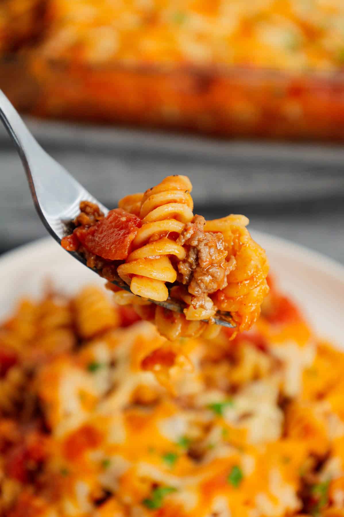 Cheeseburger Casserole is a hearty dish loaded with rotini pasta, ground beef, diced red onions, diced tomatoes, cheddar soup and shredded cheddar cheese.