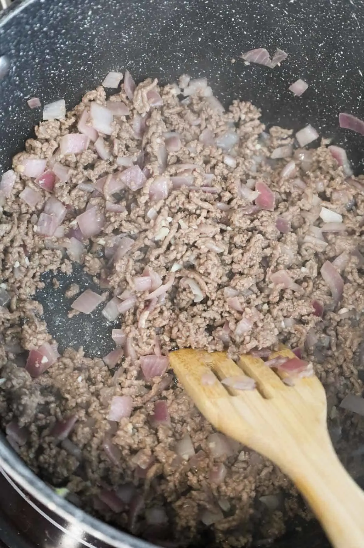 stirring minced garlic with ground beef and diced onions