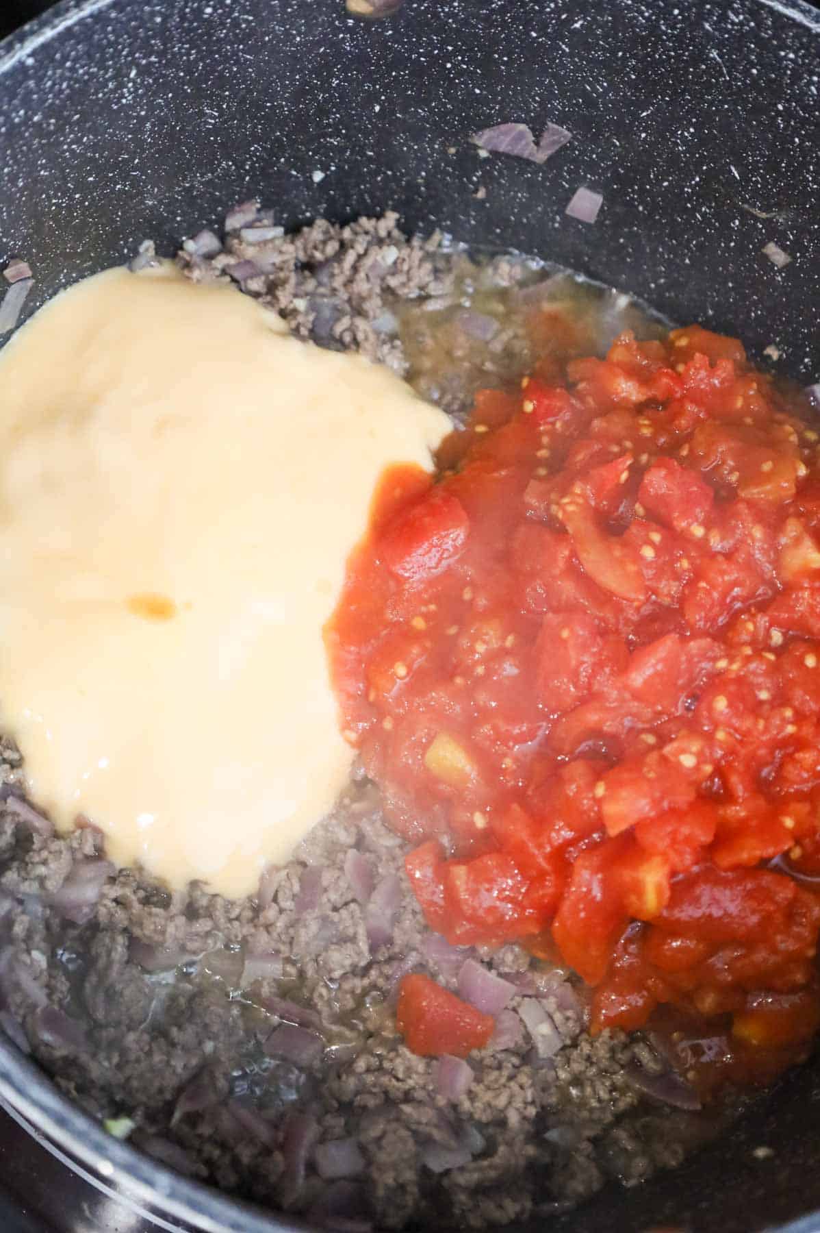 condensed cheddar soup and diced tomatoes on top of cooked ground beef in a pot