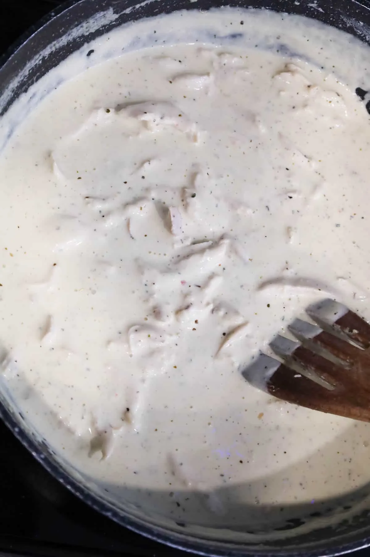 shredded chicken being stirred into cream sauce in a skillet